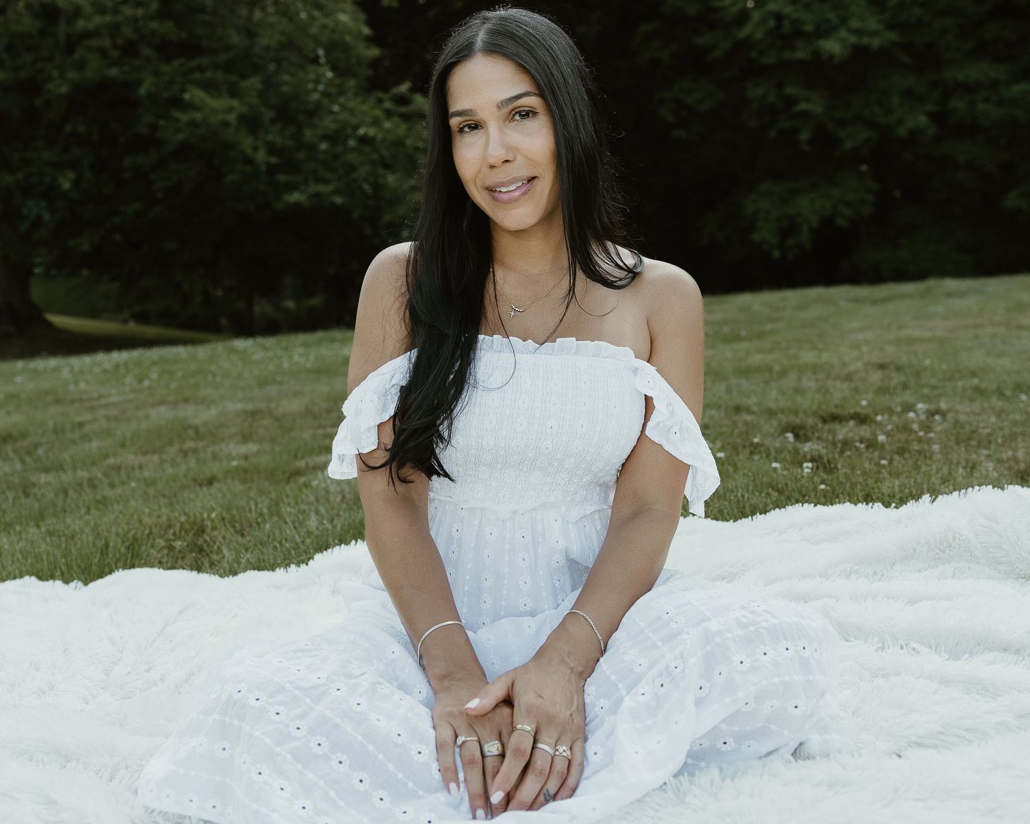 Woman in white off-shoulder eyelet dress seated on grass during golden hour portrait session in Woodbridge CT