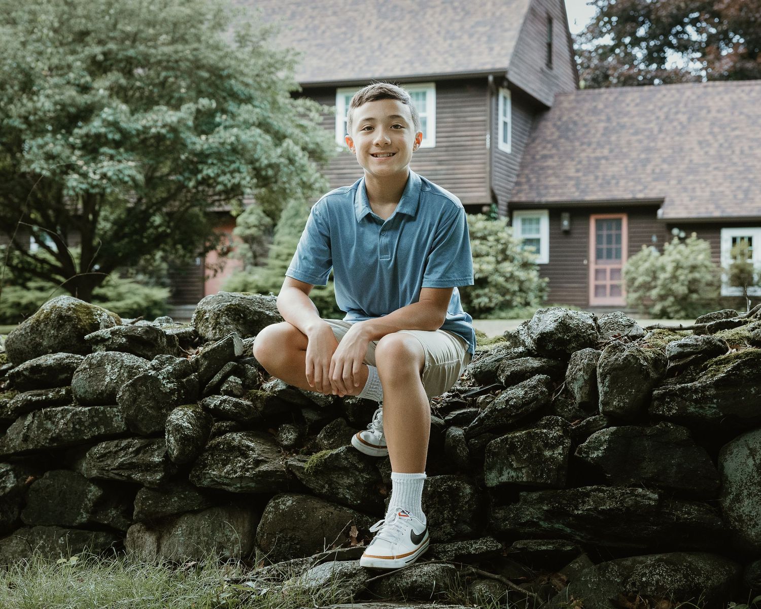 Teenage boy sitting on a stone wall during a family portrait session in Woodbridge, CT
