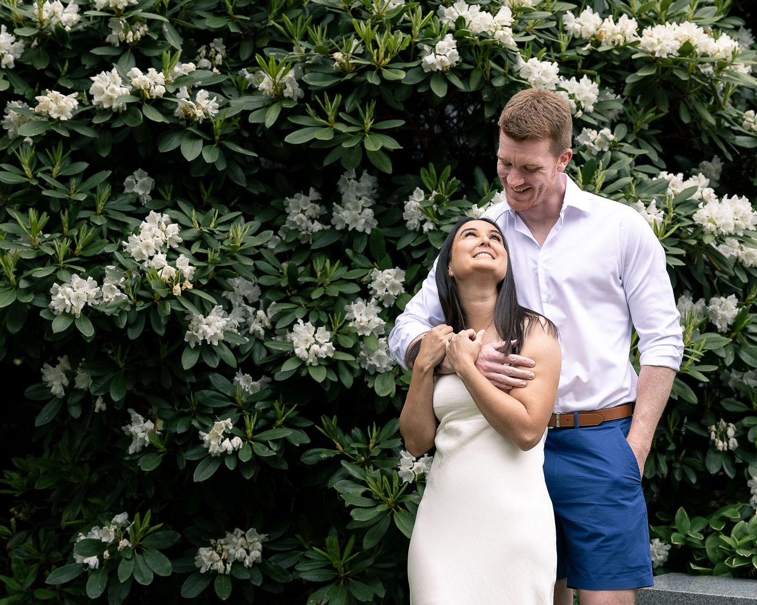 Engaged couple embracing in front of a blooming rhododendron bush, elopement photography New Haven County CT