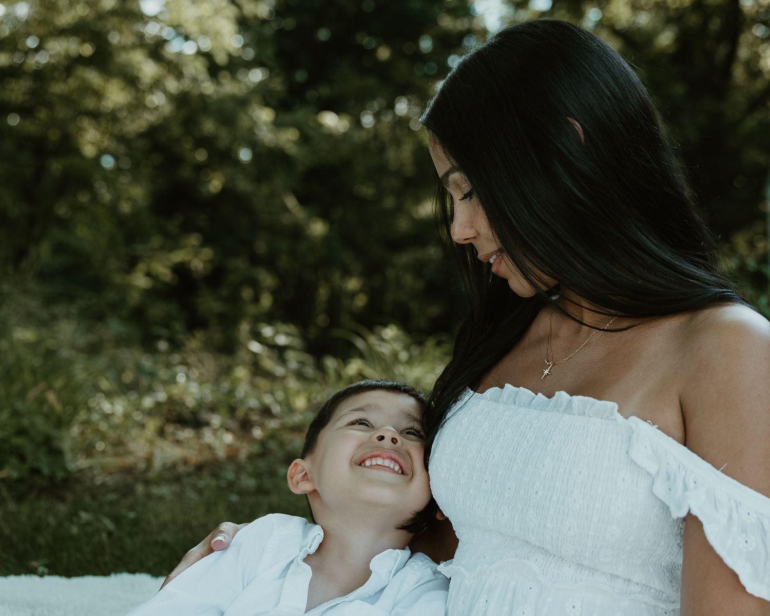 Mother and son laughing together in white outfits on a blanket outdoors, New Haven County CT
