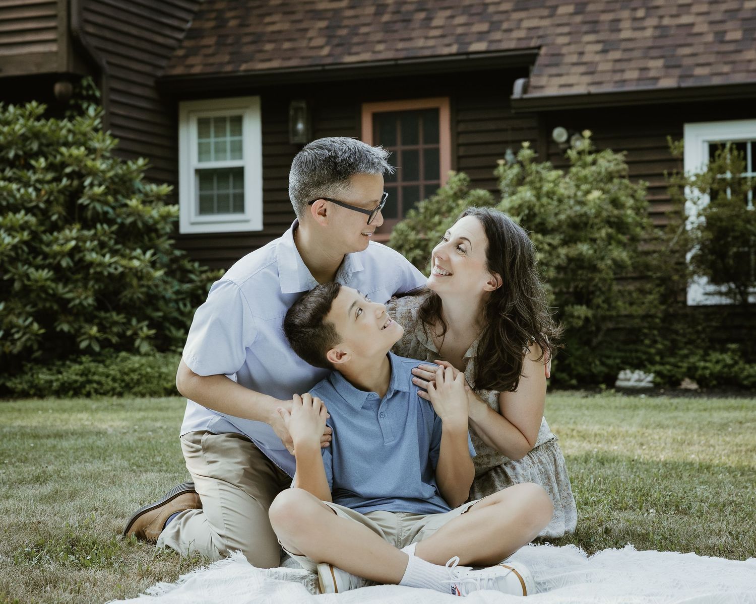 Family portrait photographer in Woodbridge CT capturing a mother and father embracing their teenage son on a picnic blanket