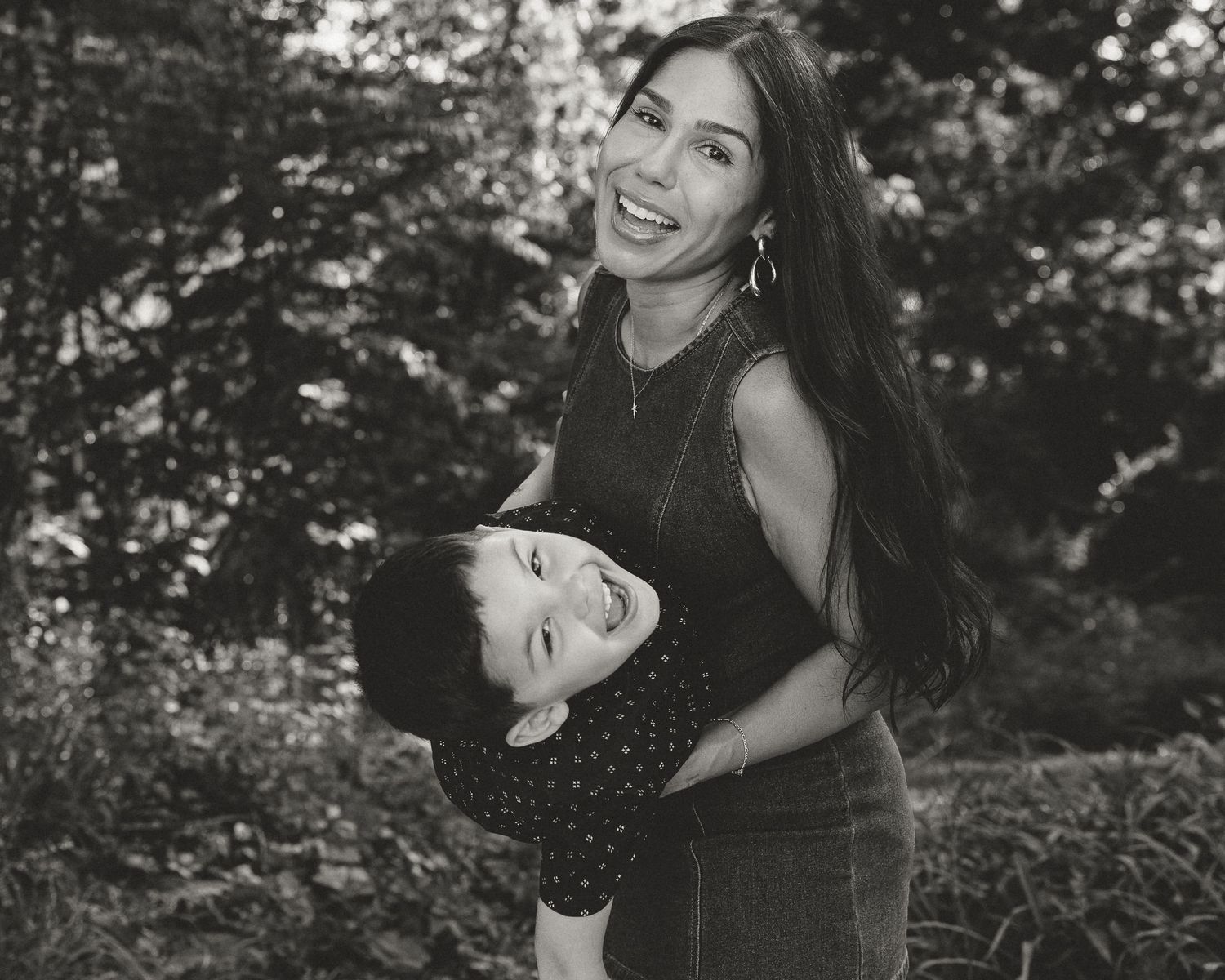 Mother holding her young son upside down, both laughing outdoors in black and white, by a New Haven County CT family photographer