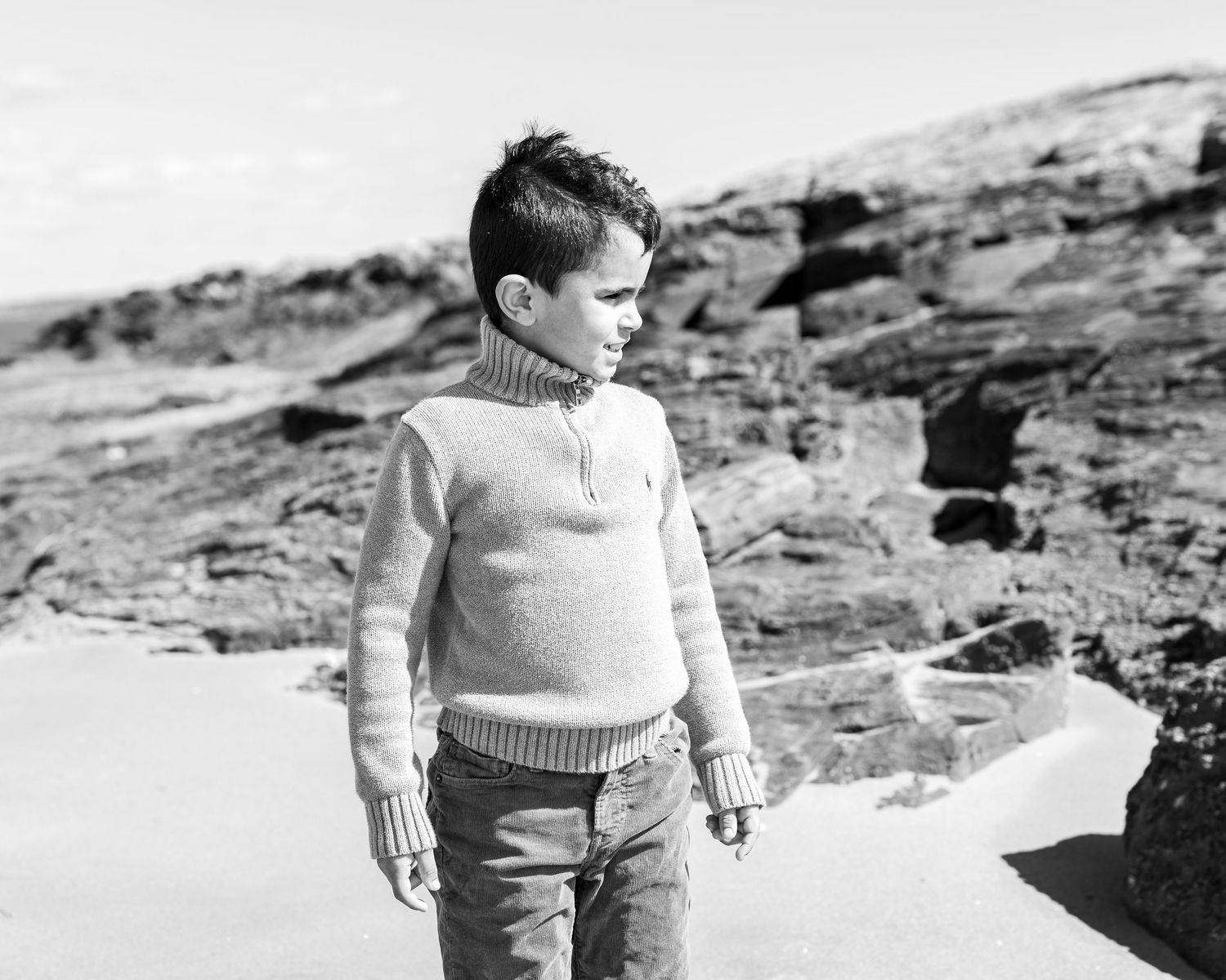 Young boy in sweater standing on Sea Bluff beach, black and white portrait by Connecticut photographer Noemi Blumenthal Photography