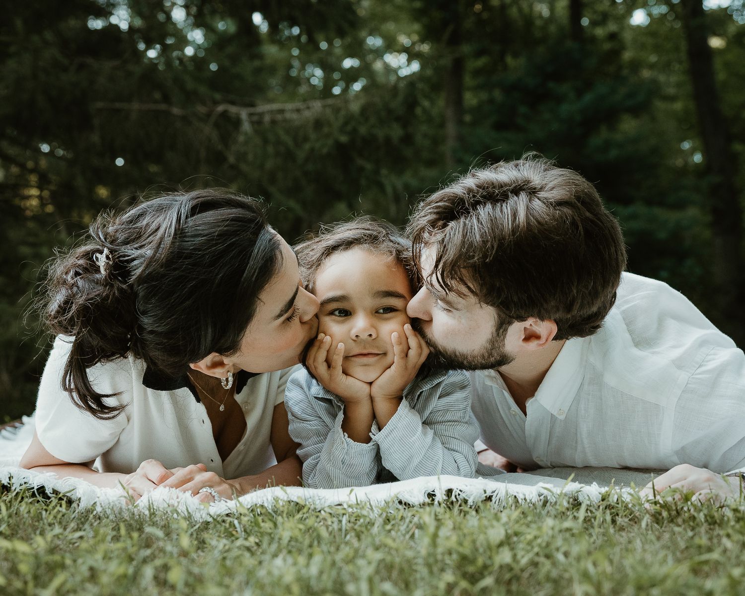 Parents kissing their child on both cheeks, outdoor family portrait in Woodbridge, CT