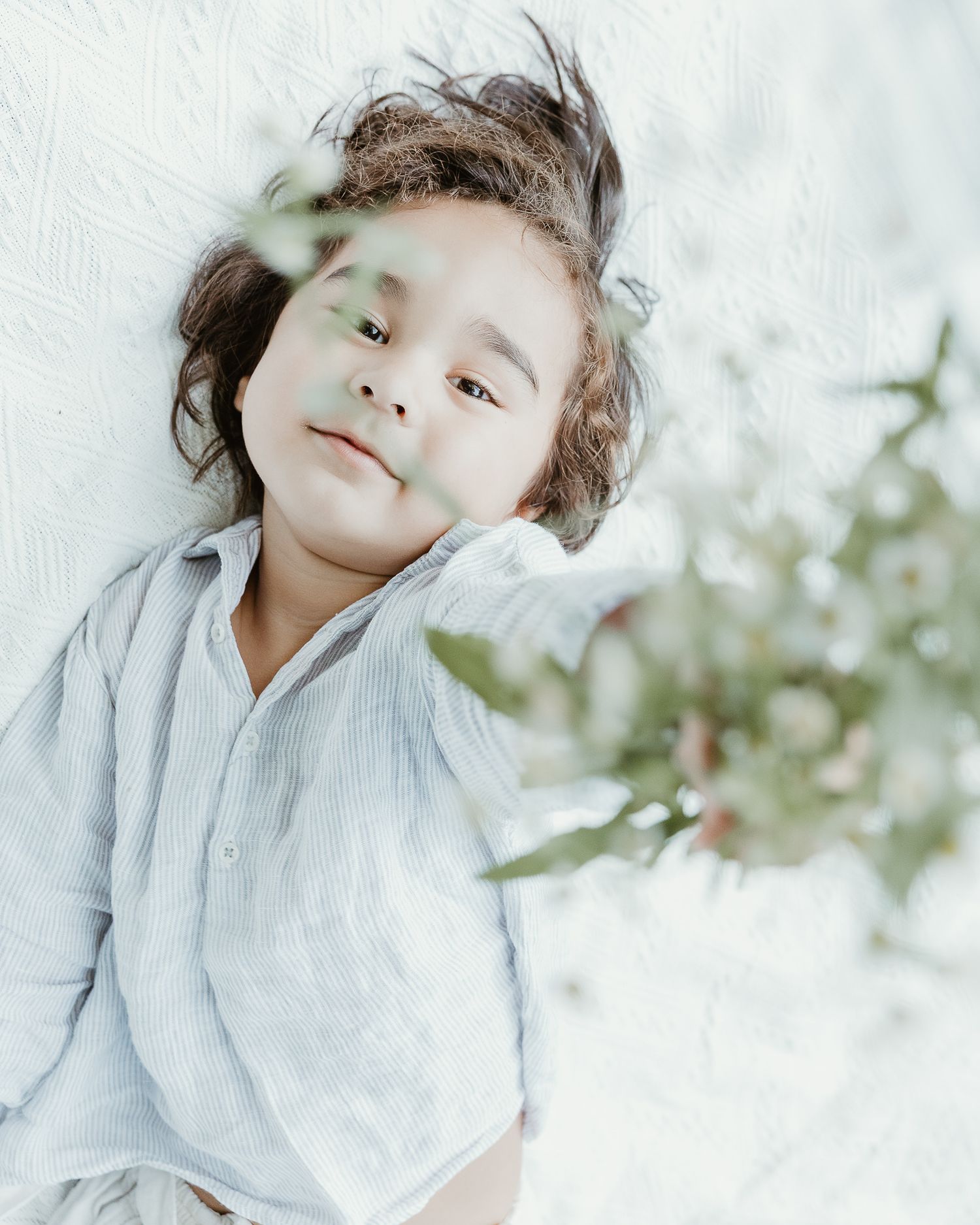 Young child lying down surrounded by soft natural light and greenery, Woodbridge, CT portrait session