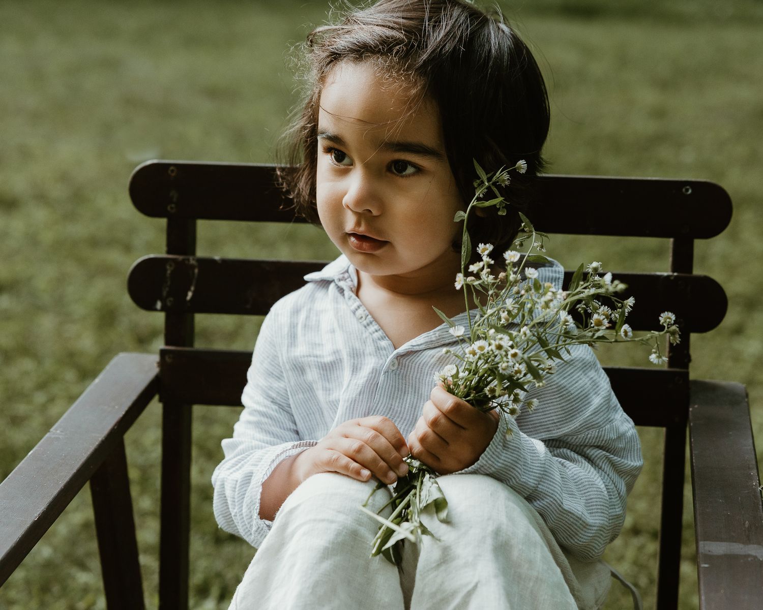 Young child seated on a bench holding a small bouquet of wildflowers, outdoor family session in Woodbridge, CT
