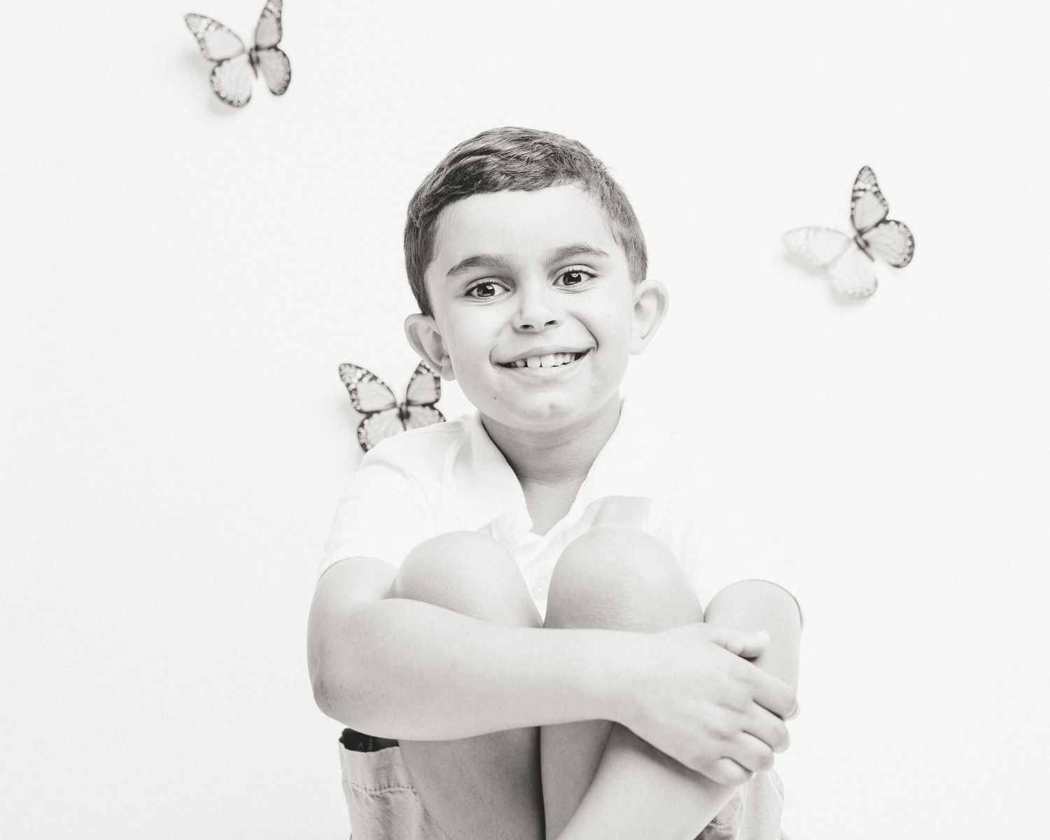 Boy smiling with hands on knees among butterflies, studio session, Connecticut children's photography