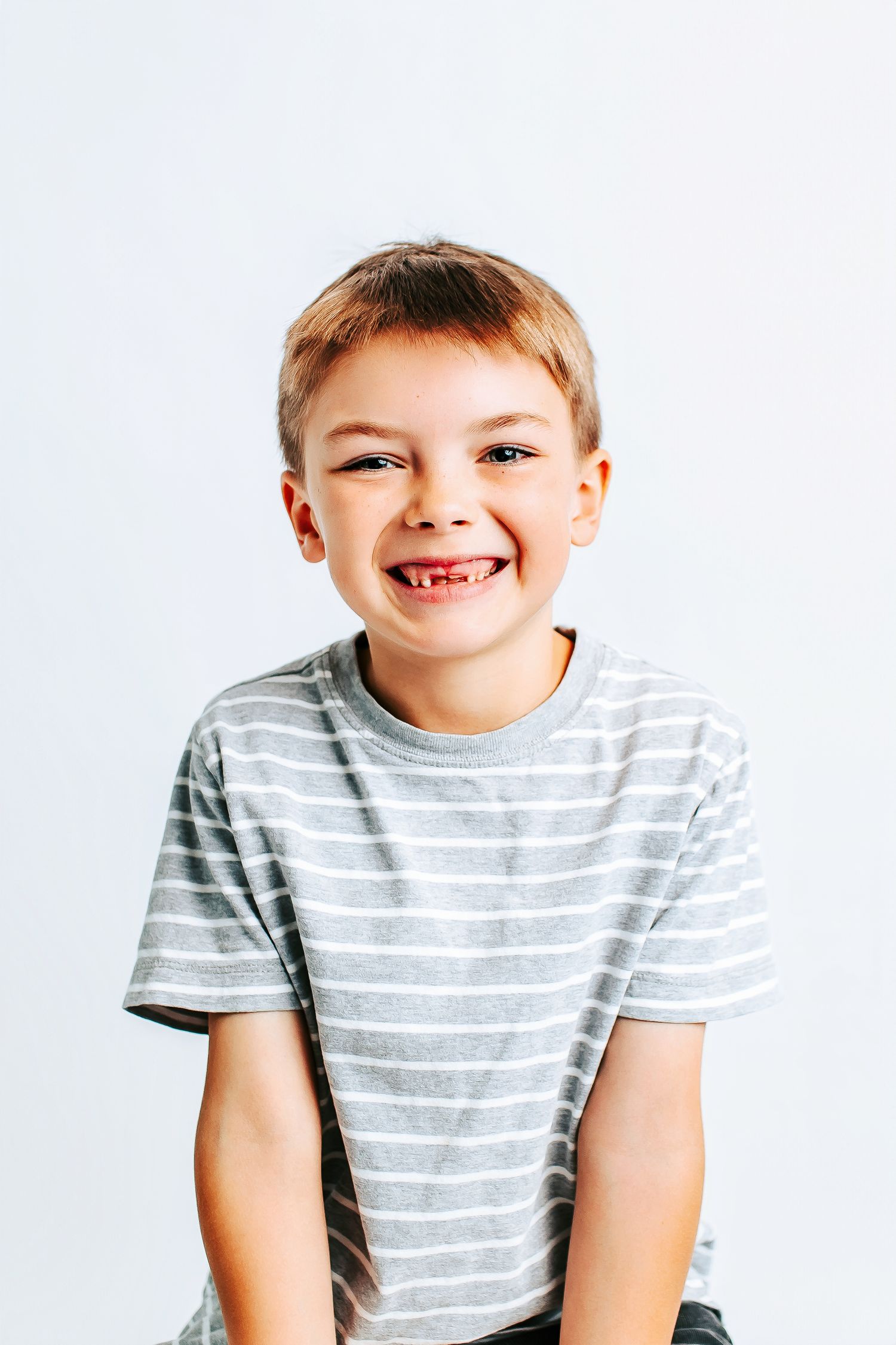 Child wearing gray and white striped t-shirt smiling against white background in three sequential poses.