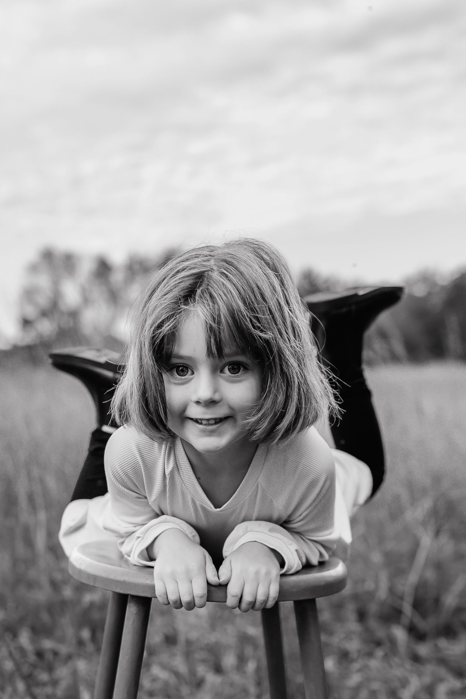 Creative black and white portrait of a child laying on a bench outdoors.