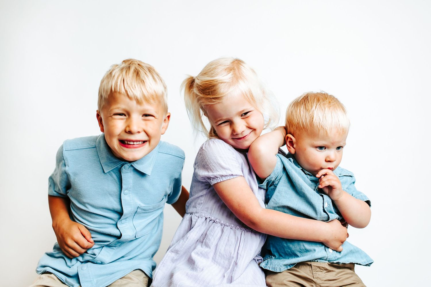 Two children in light blue shirts sit together and laugh playfully while posing for photos.