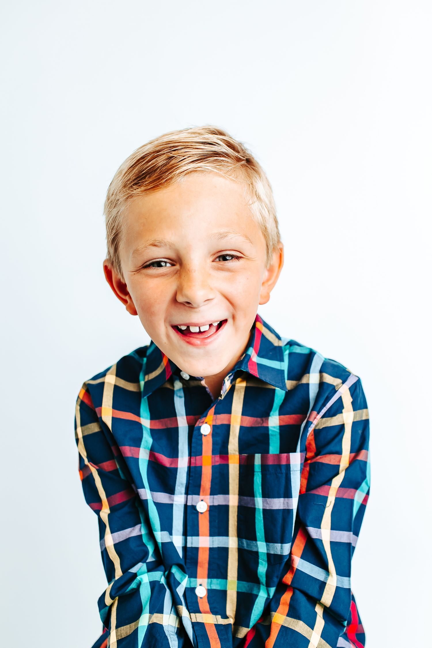 Young child wearing colorful plaid shirt smiling and showing playful expressions in studio portraits.