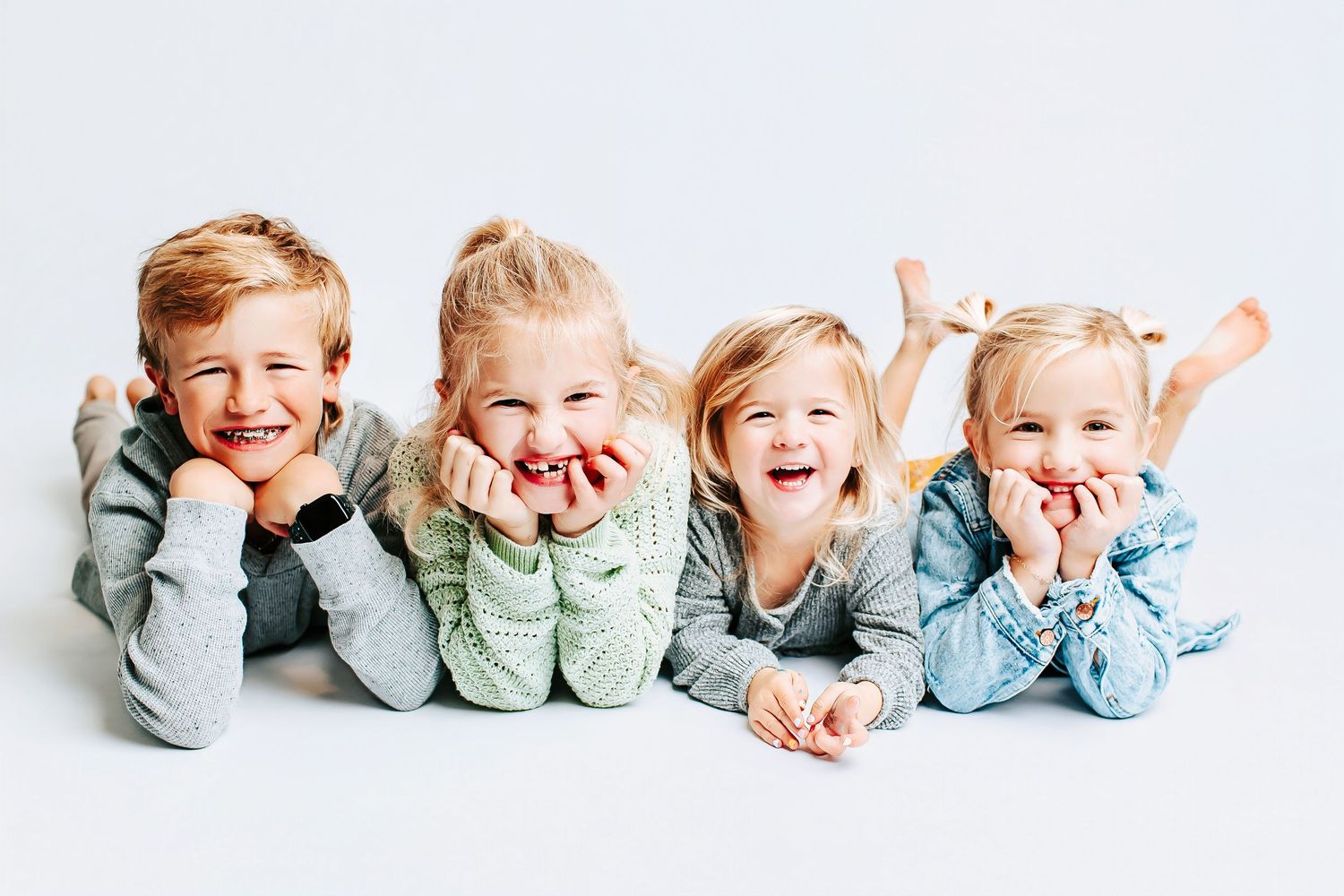 Children in matching blue outfits lying in a row for a playful studio portrait.
