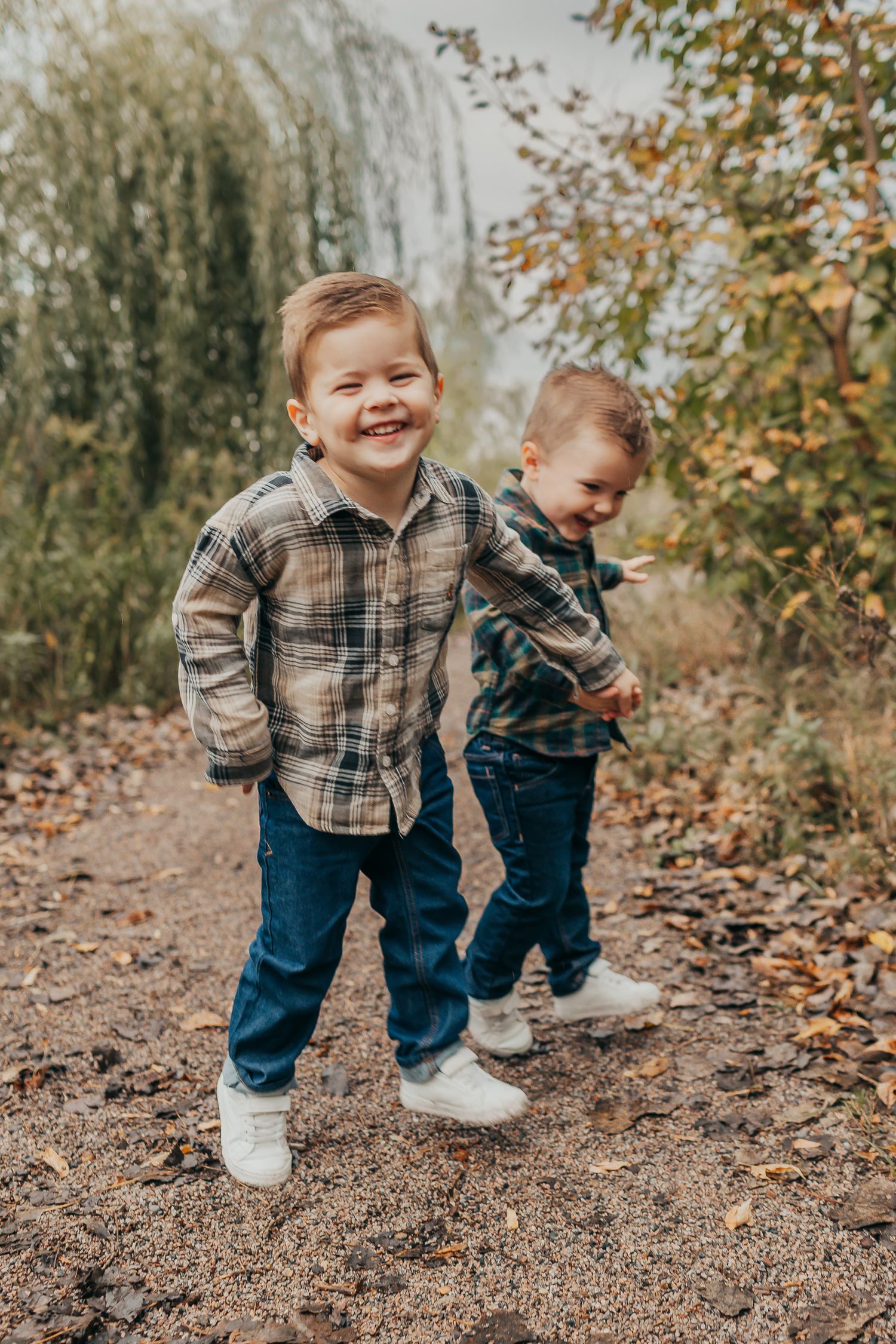 Two young children in plaid shirts and jeans playing together on a path covered in autumn leaves.