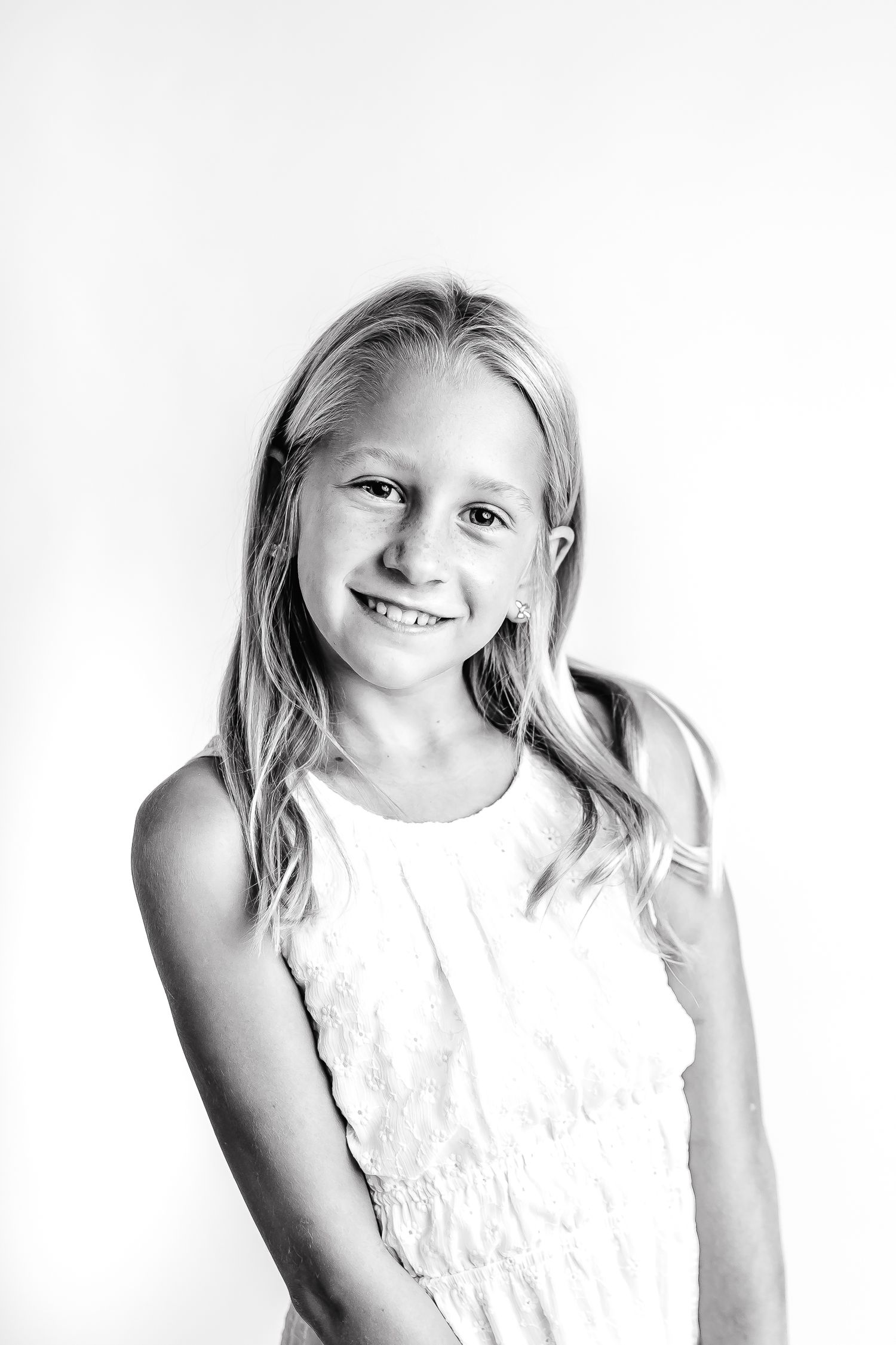 A series of three black and white portraits showing a young child in a white dress making playful expressions.