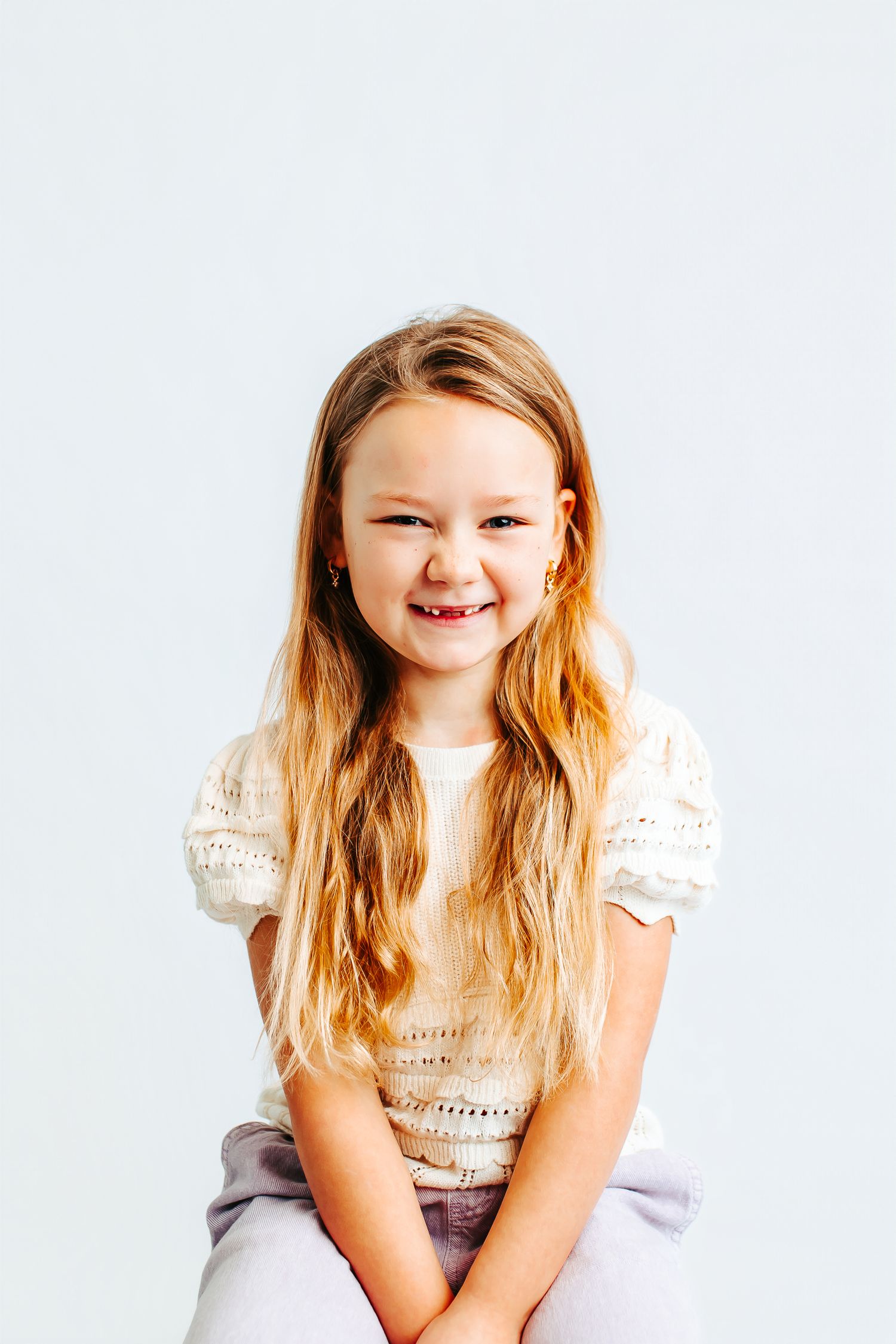 Child wearing cream lace top smiling and posing against white background.