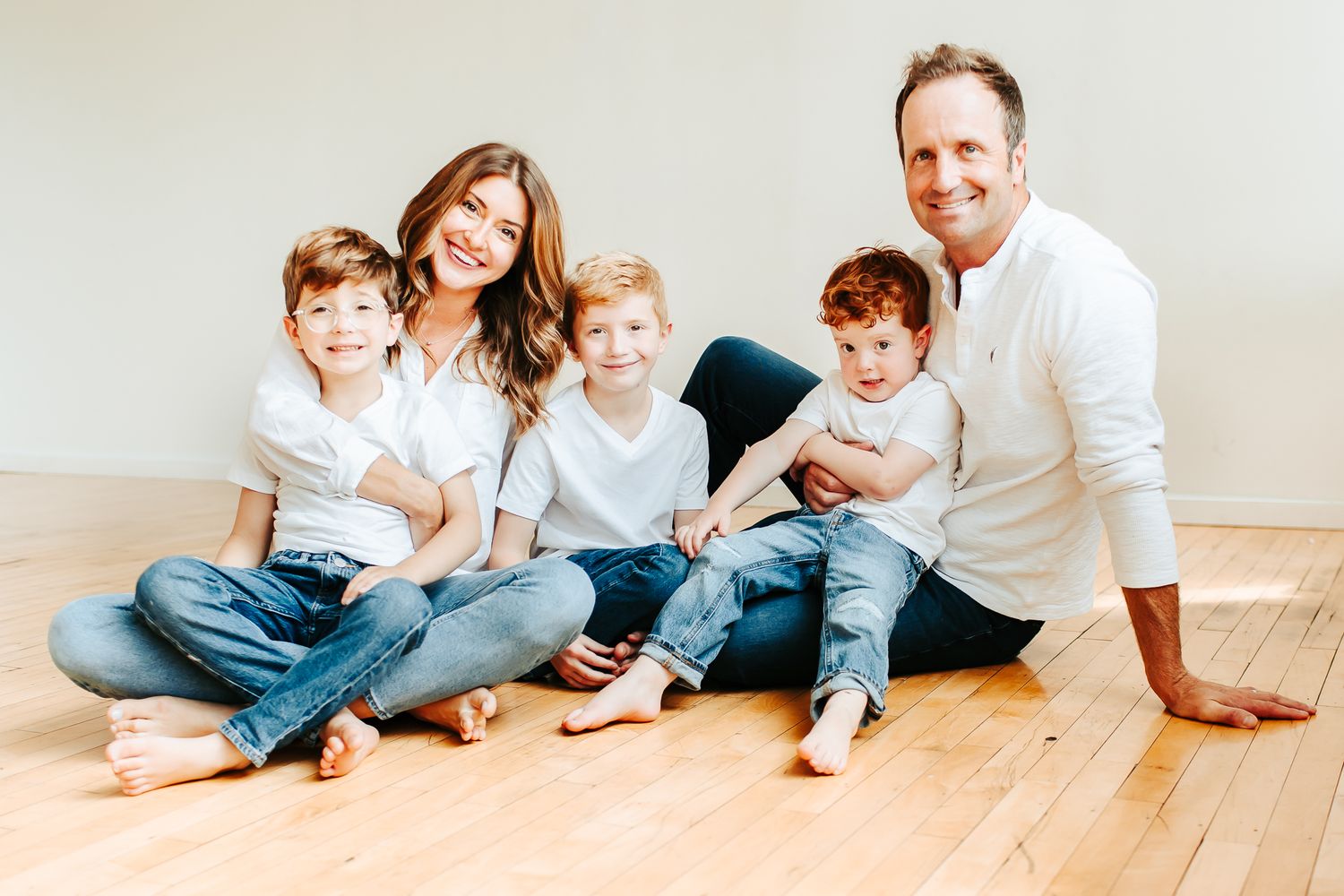 Family in white and denim casual wear relaxing together on hardwood floor.