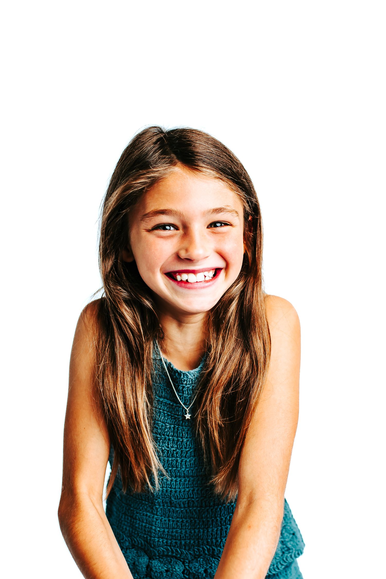 Child in teal dress making playful expressions in studio photoshoot.