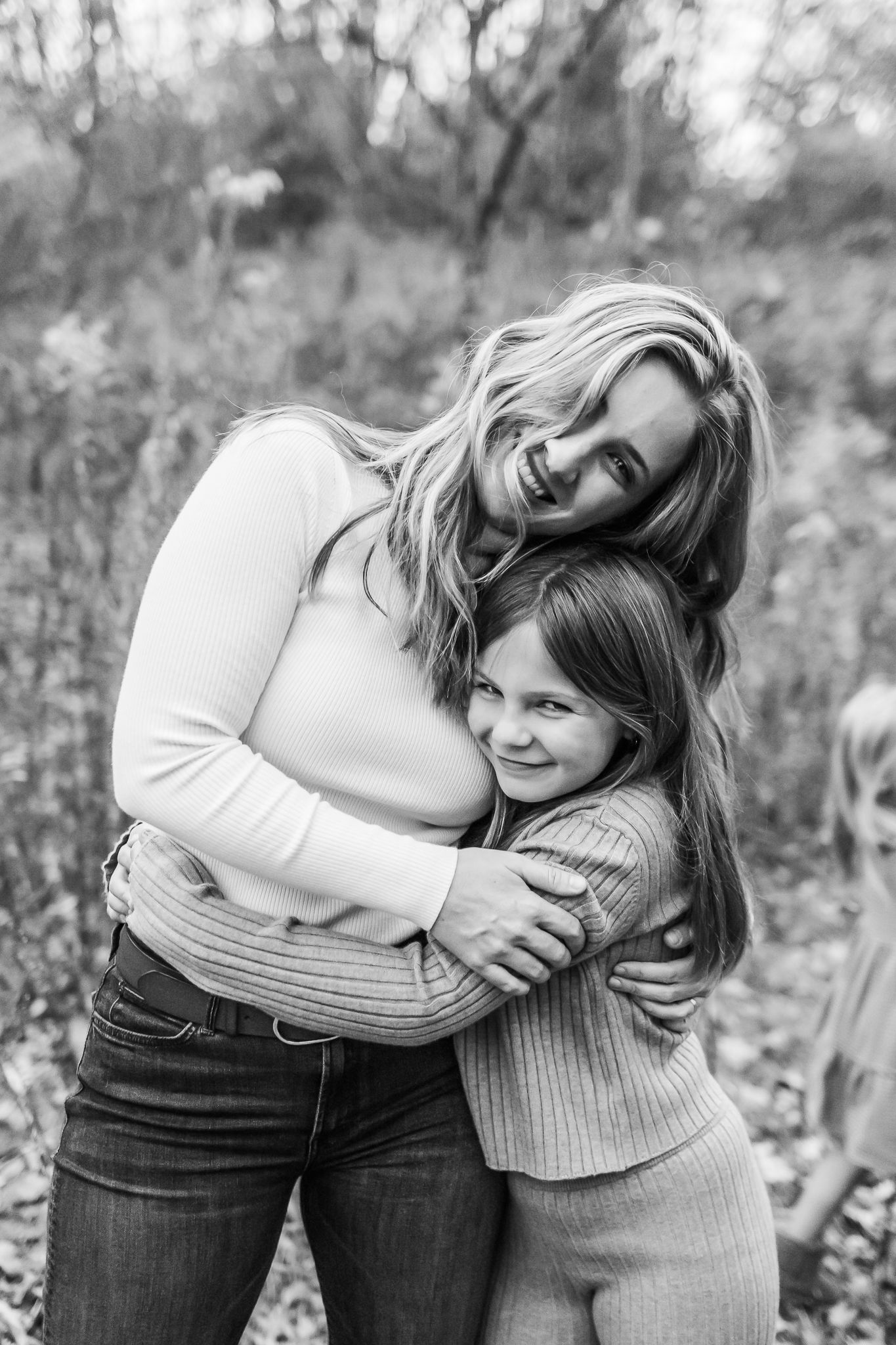 A black and white portrait showing two people sharing a warm embrace outdoors.