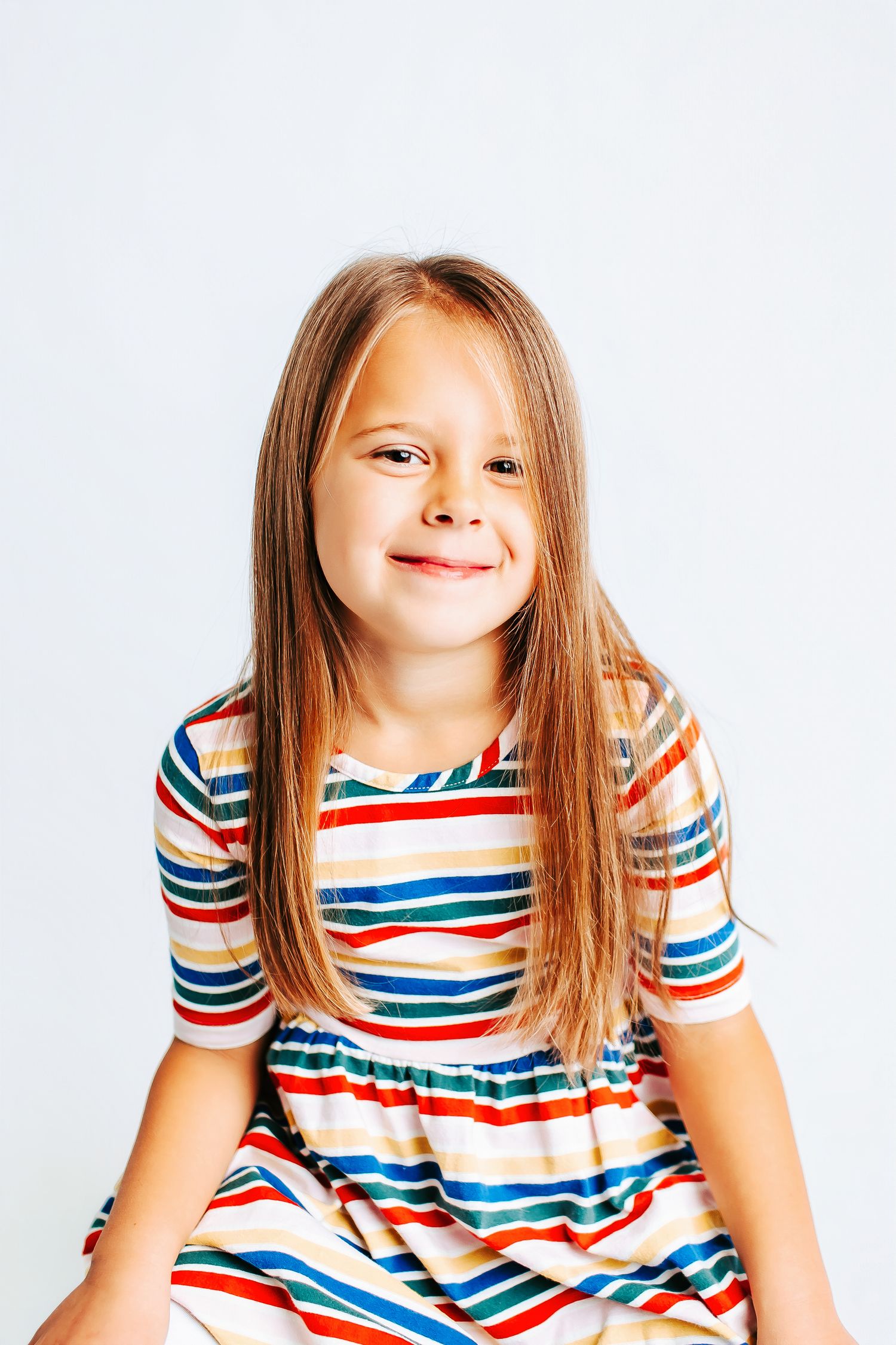 Child wearing colorful striped dress smiling and posing in studio setting.