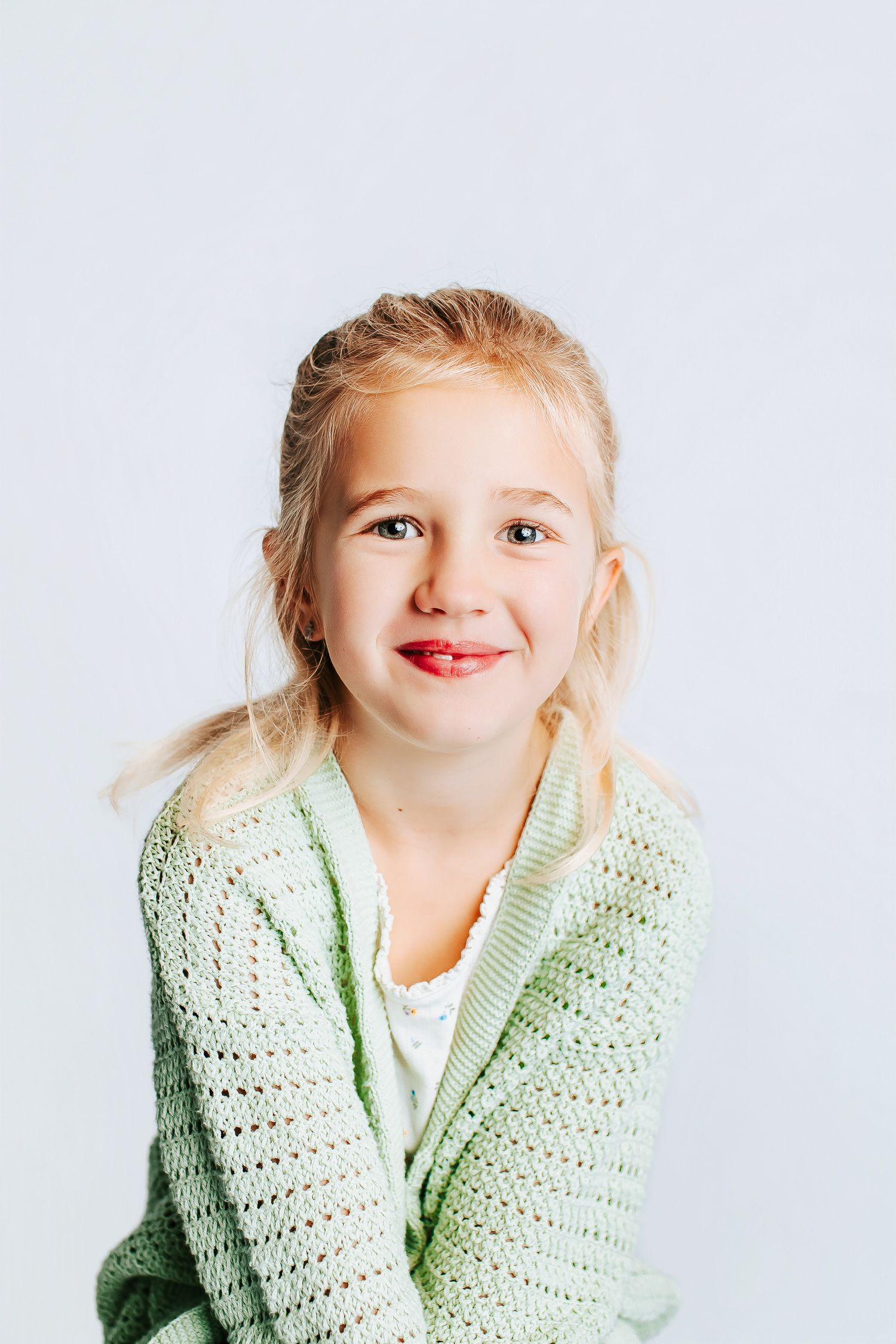 A series of portrait shots showing a child wearing a mint green knitted sweater against a white background.