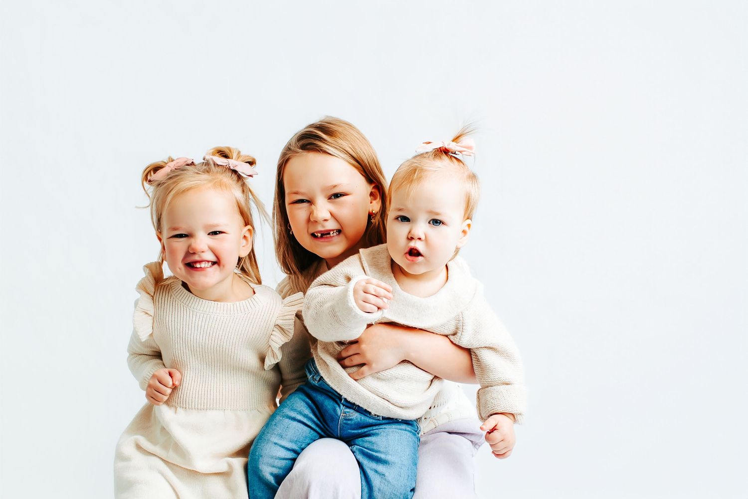 Infants in white clothing sit and laugh together while playing on a light-colored background.
