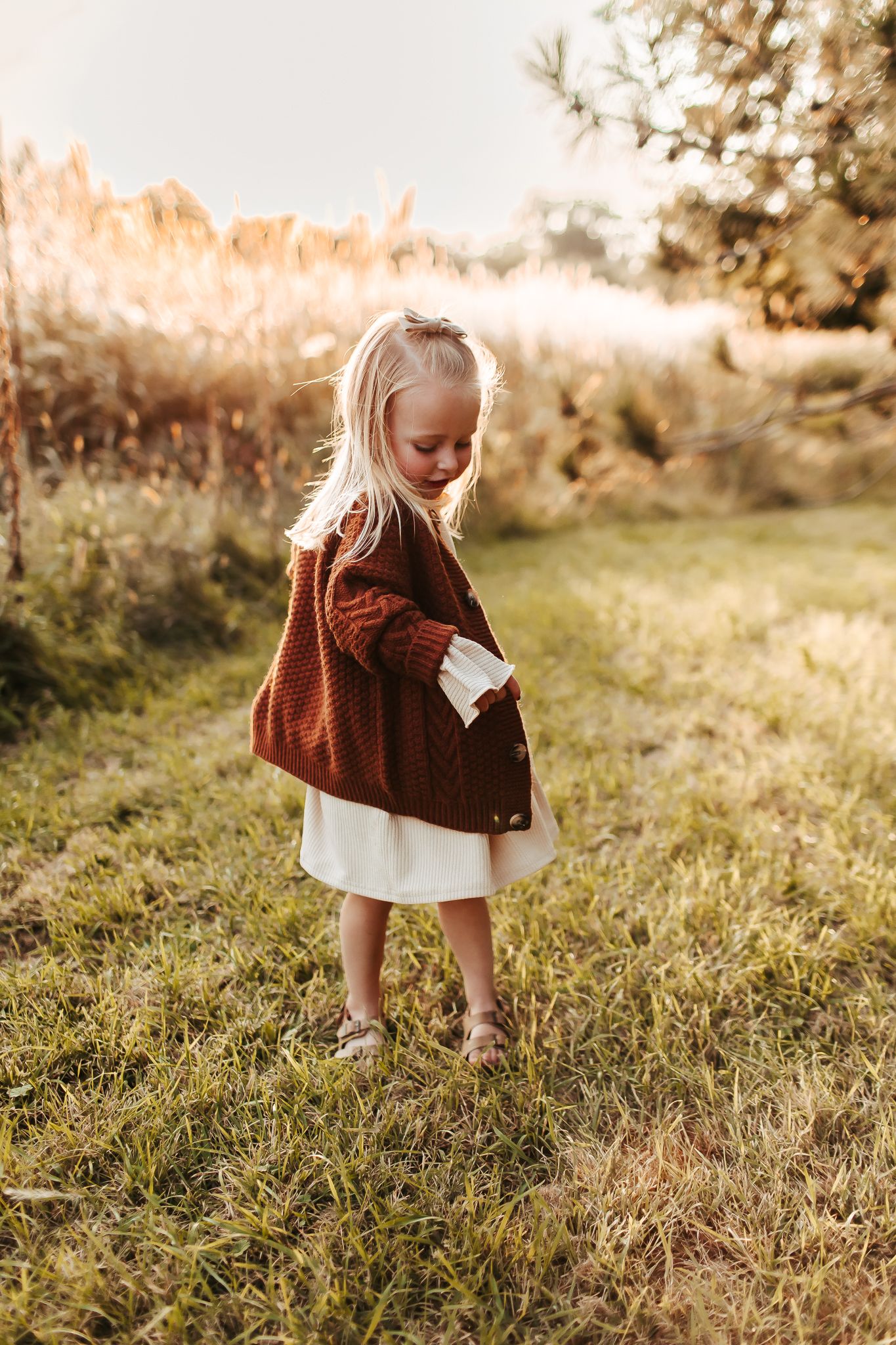 Child in a brown sweater exploring a sunlit meadow during golden hour.