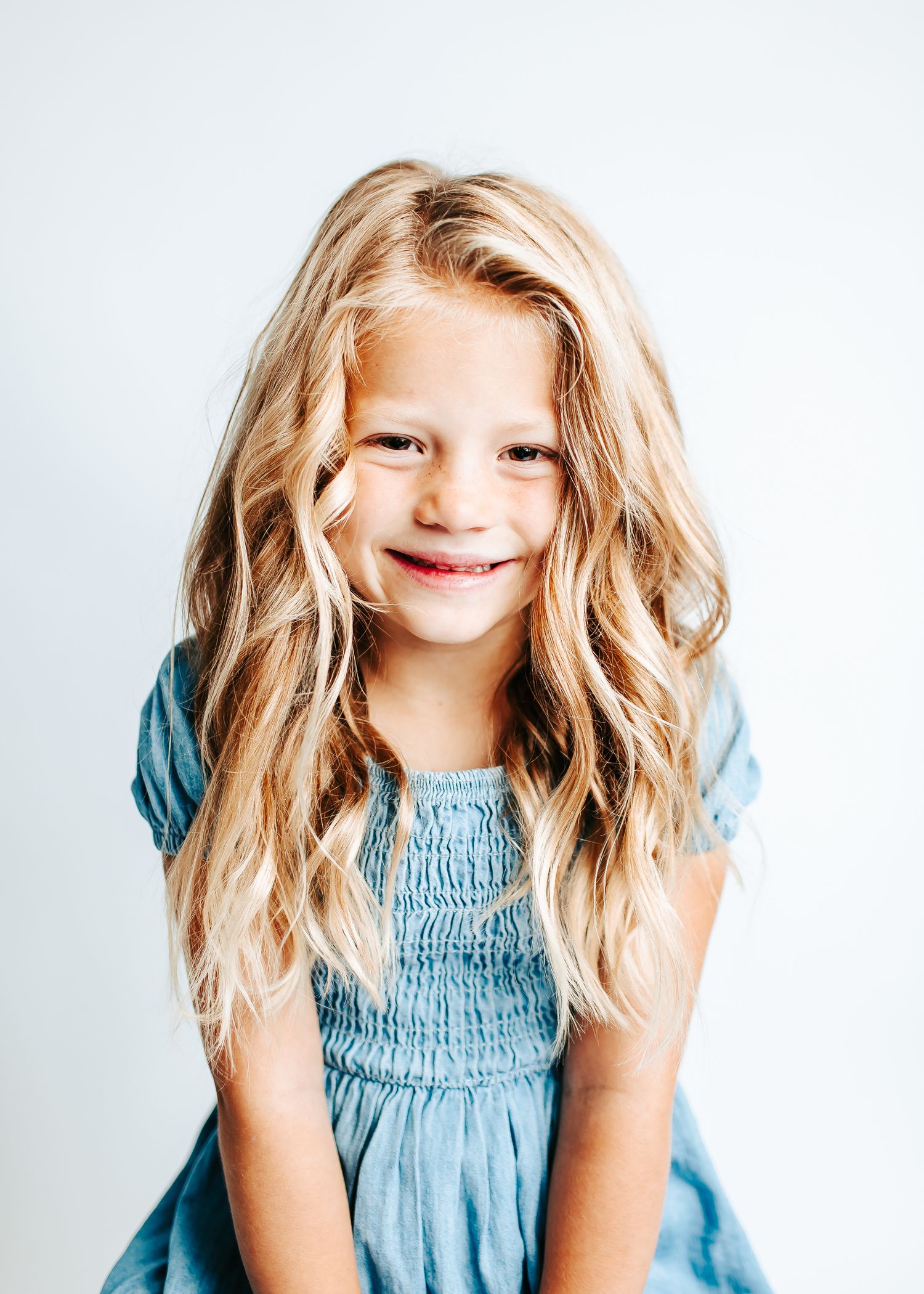 Young child in light blue smocked dress smiling and posing against white background.