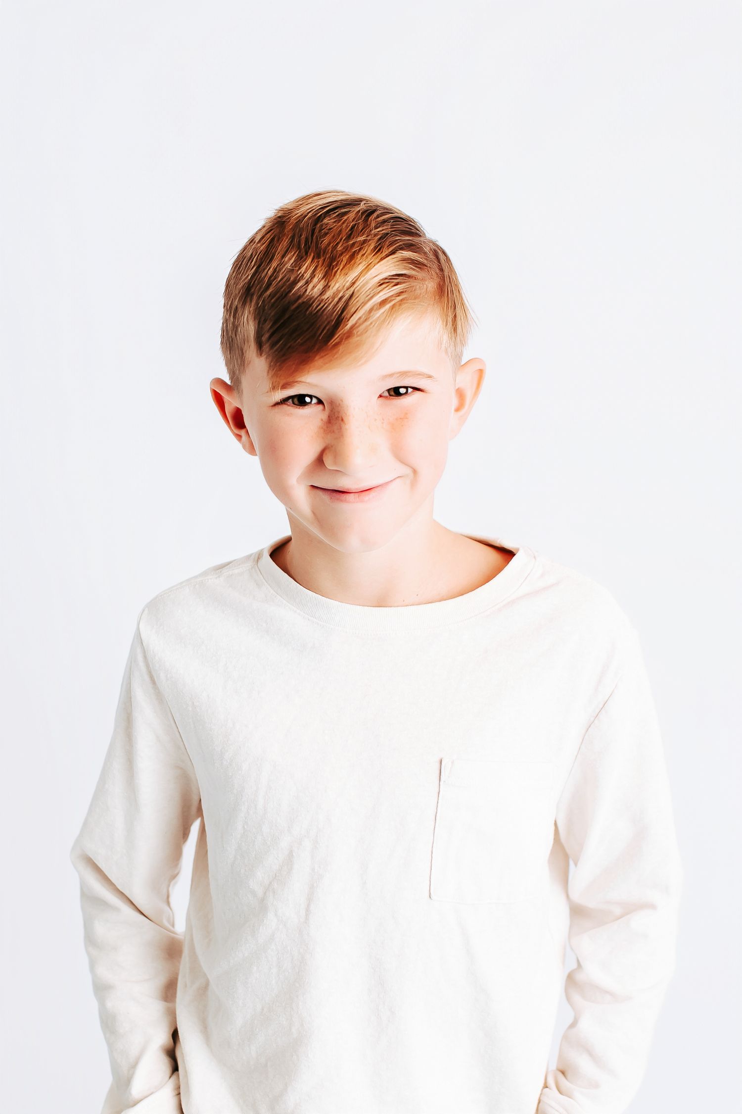 Child in white long sleeve shirt making silly faces against white background.