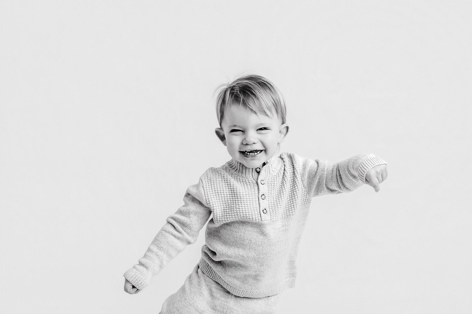 Energetic child in gray sweater jumps and plays against white background.