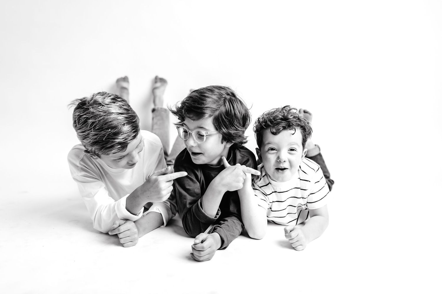 Three children lying on their stomachs in a black and white studio portrait.