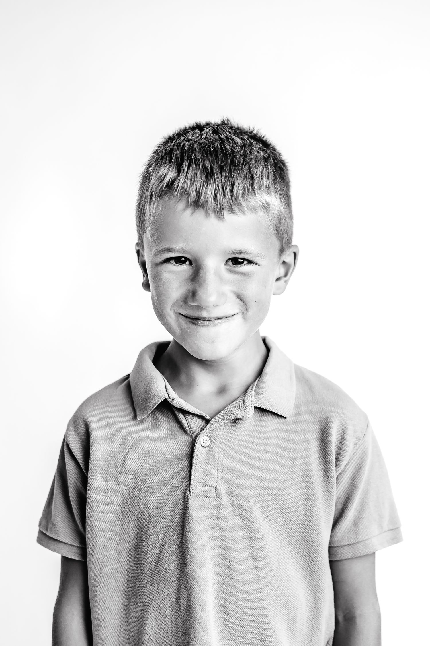 Black and white portrait of three young children wearing polo shirts and smiling at the camera.
