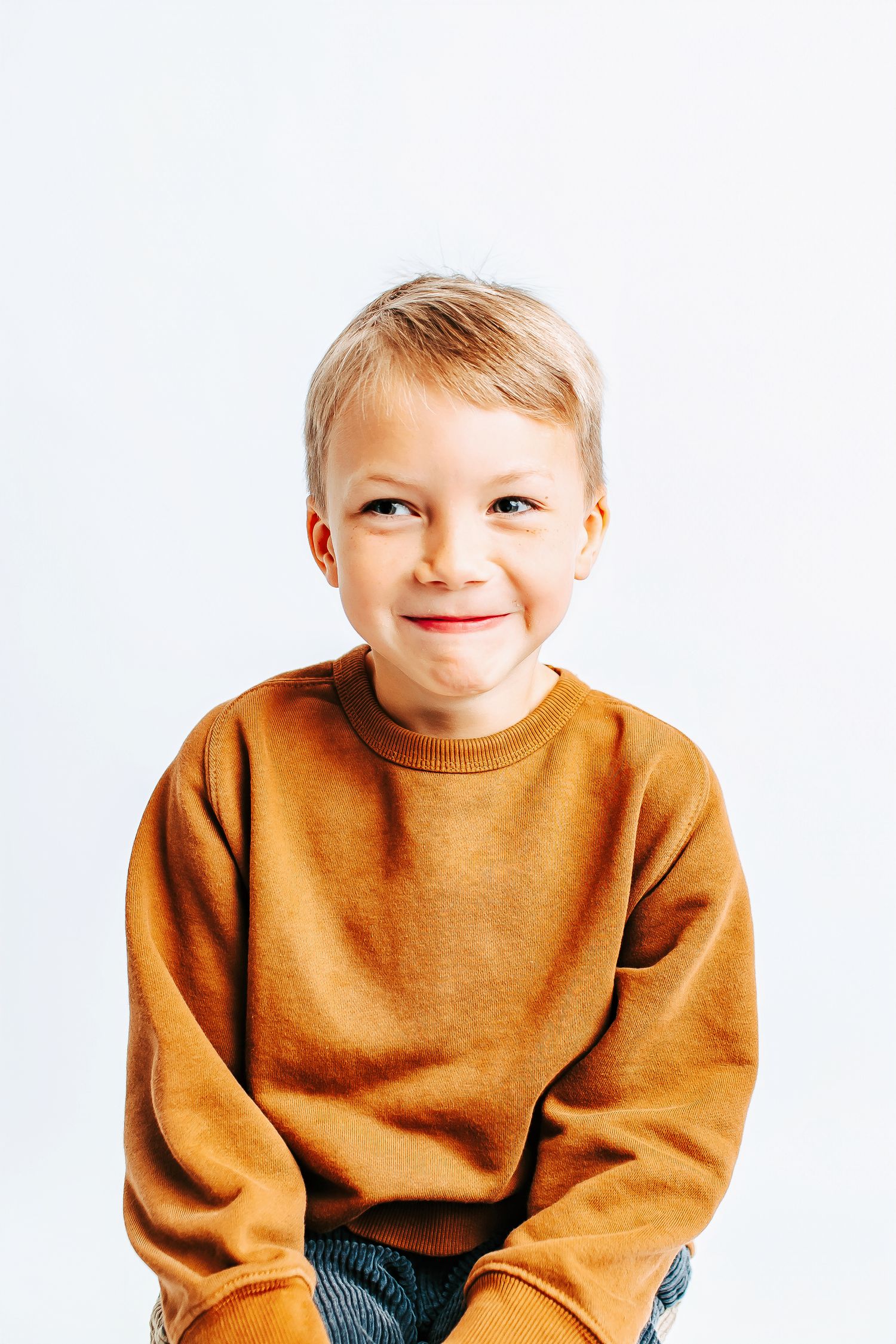 Child wearing brown sweater smiling and posing against white backdrop.