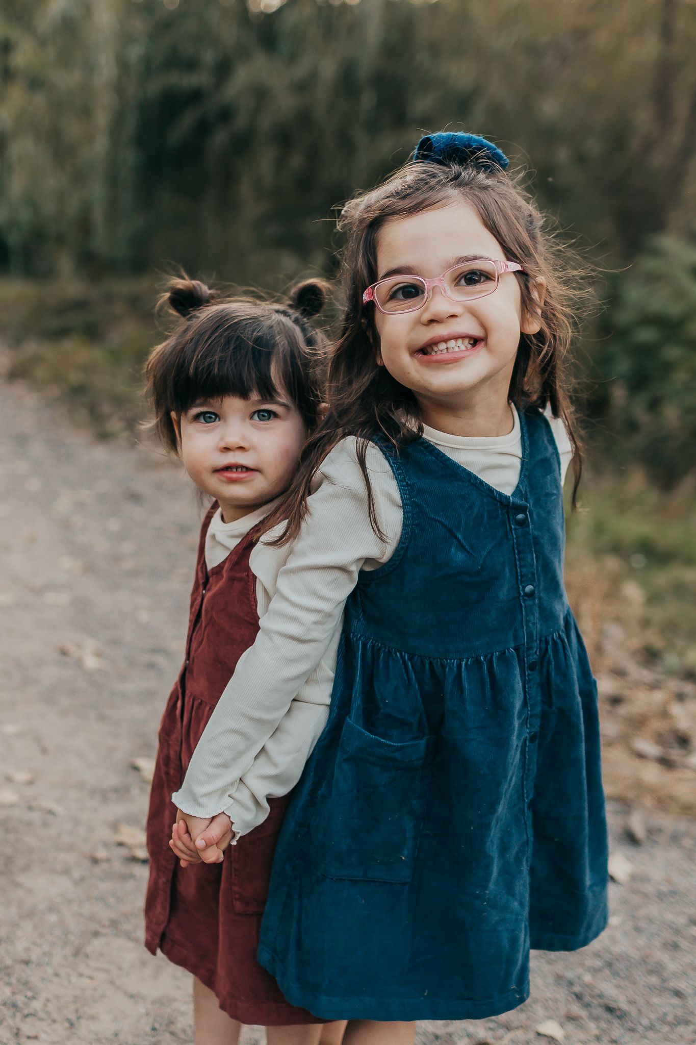 Two young children in corduroy dresses playing together outdoors in natural lighting.