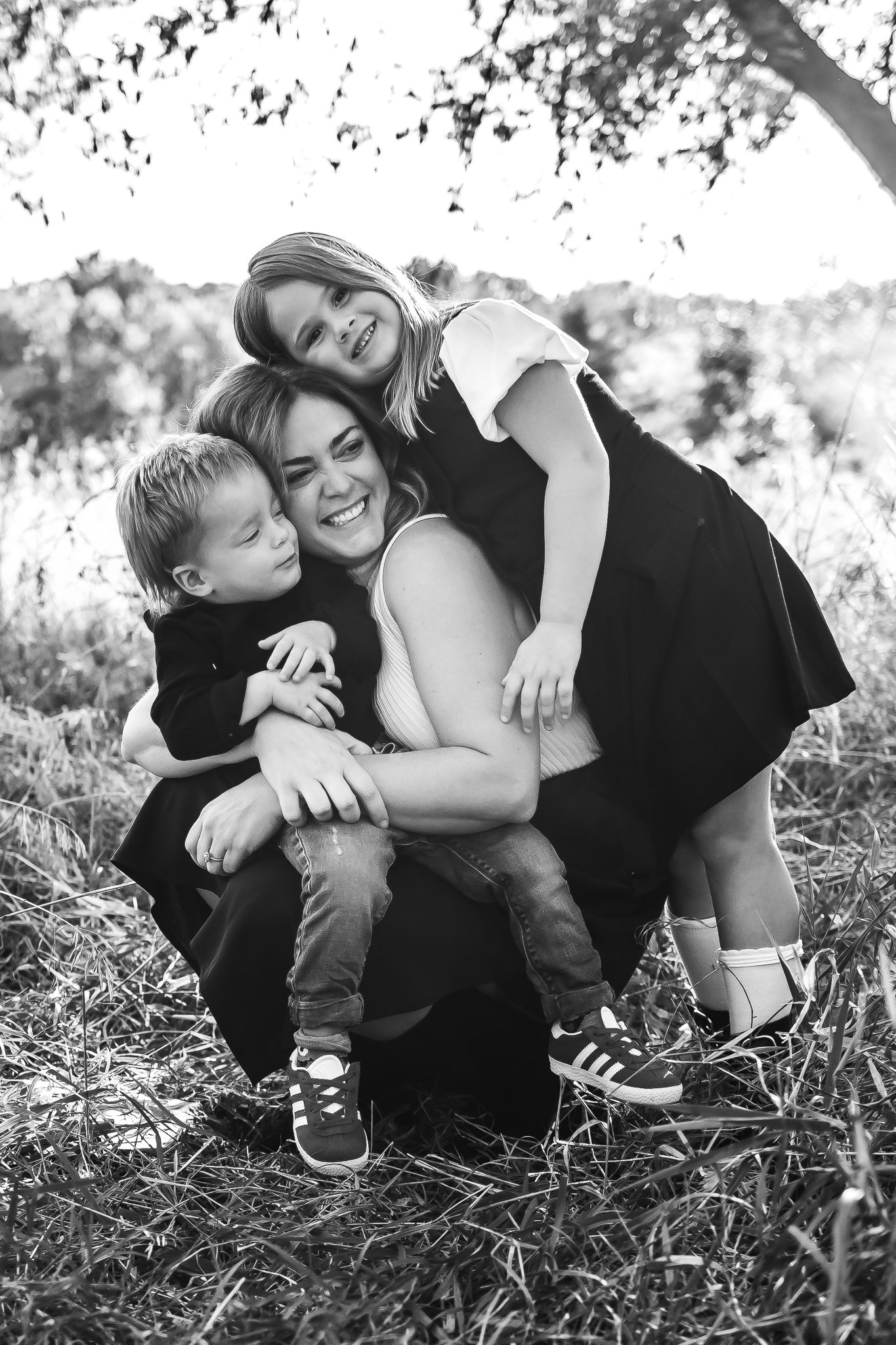 A black and white photo sequence of family members embracing on grass under trees.