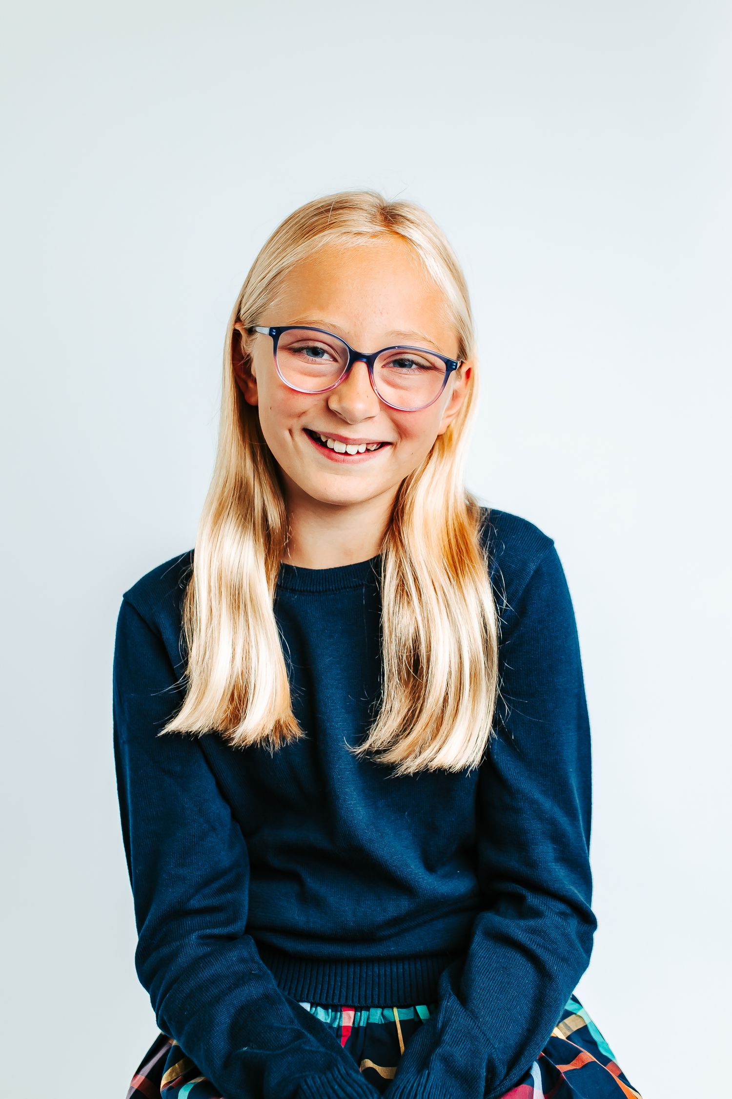 Playful poses in a navy sweater with glasses against white backdrop.