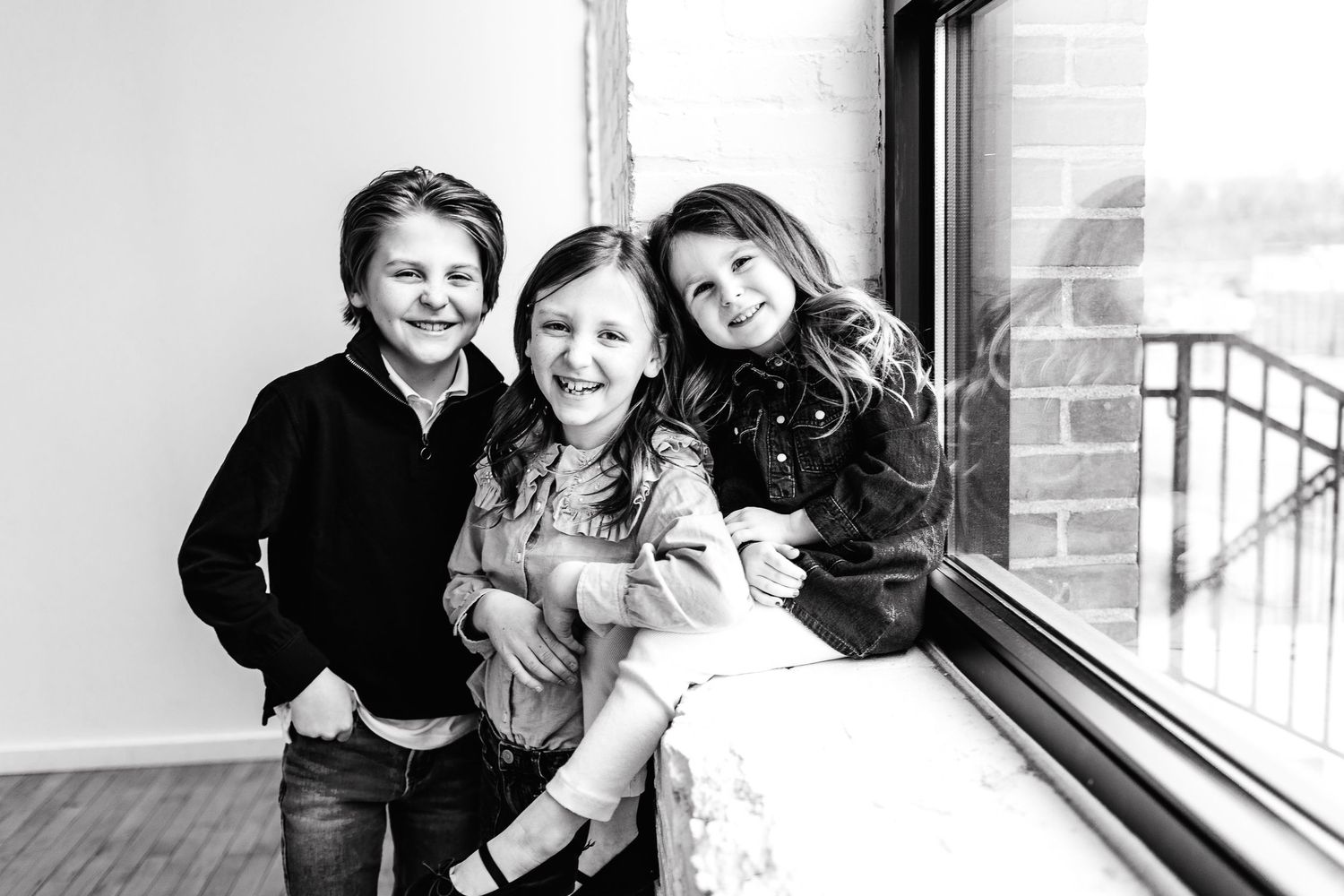 Black and white indoor family portraits showing joyful moments by a window.
