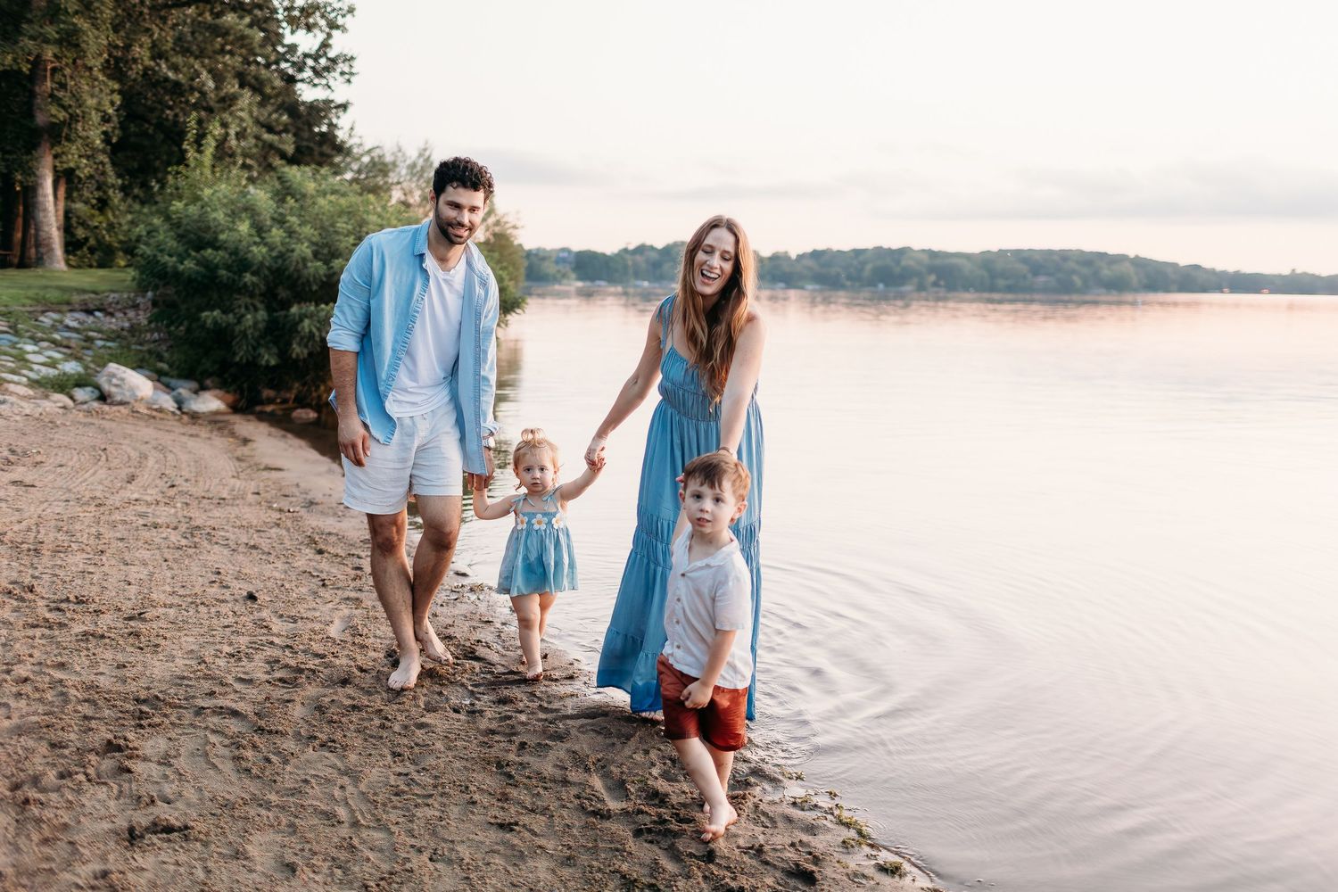 Family walking along a scenic beach shoreline at sunset wearing coordinated blue and white outfits.