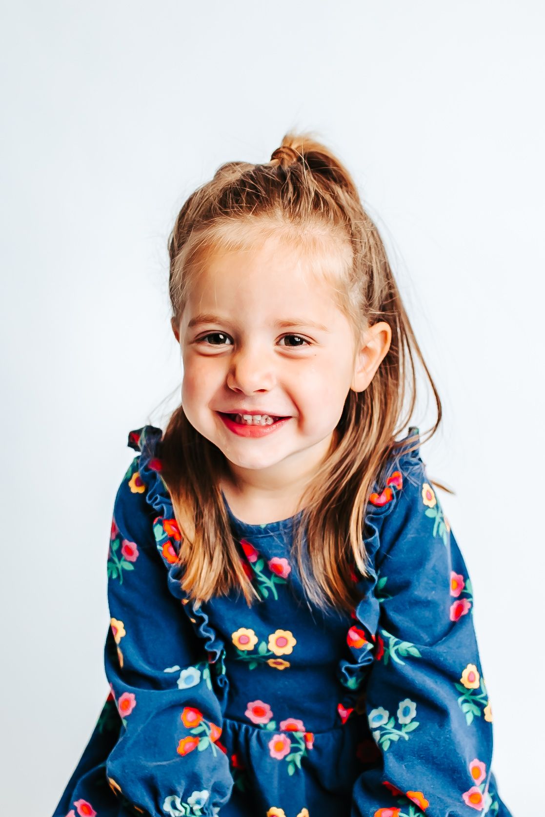A child in a blue floral dress smiles and poses playfully against a white background.