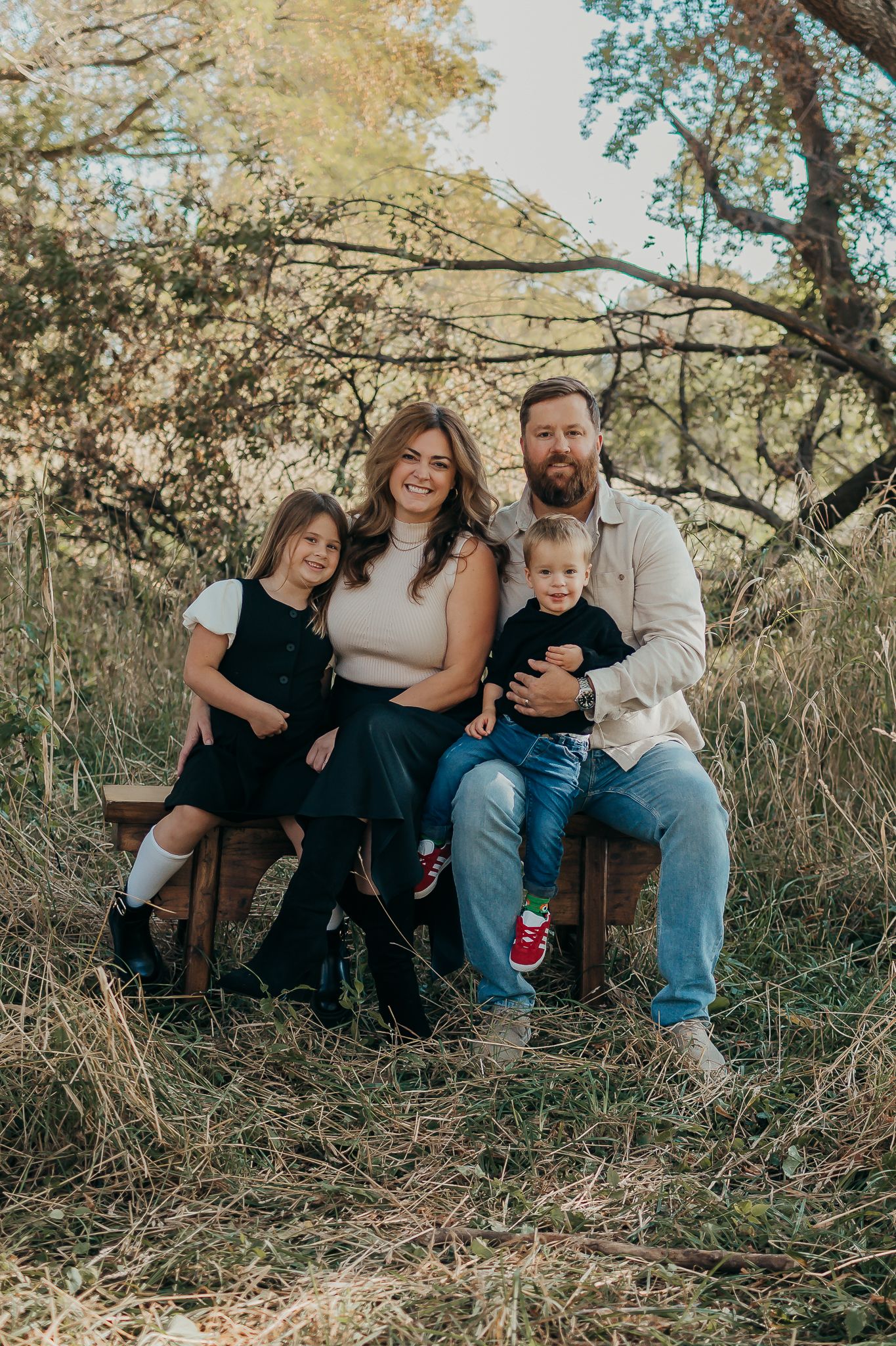 A family sits together on fallen logs in a natural outdoor setting during golden hour.