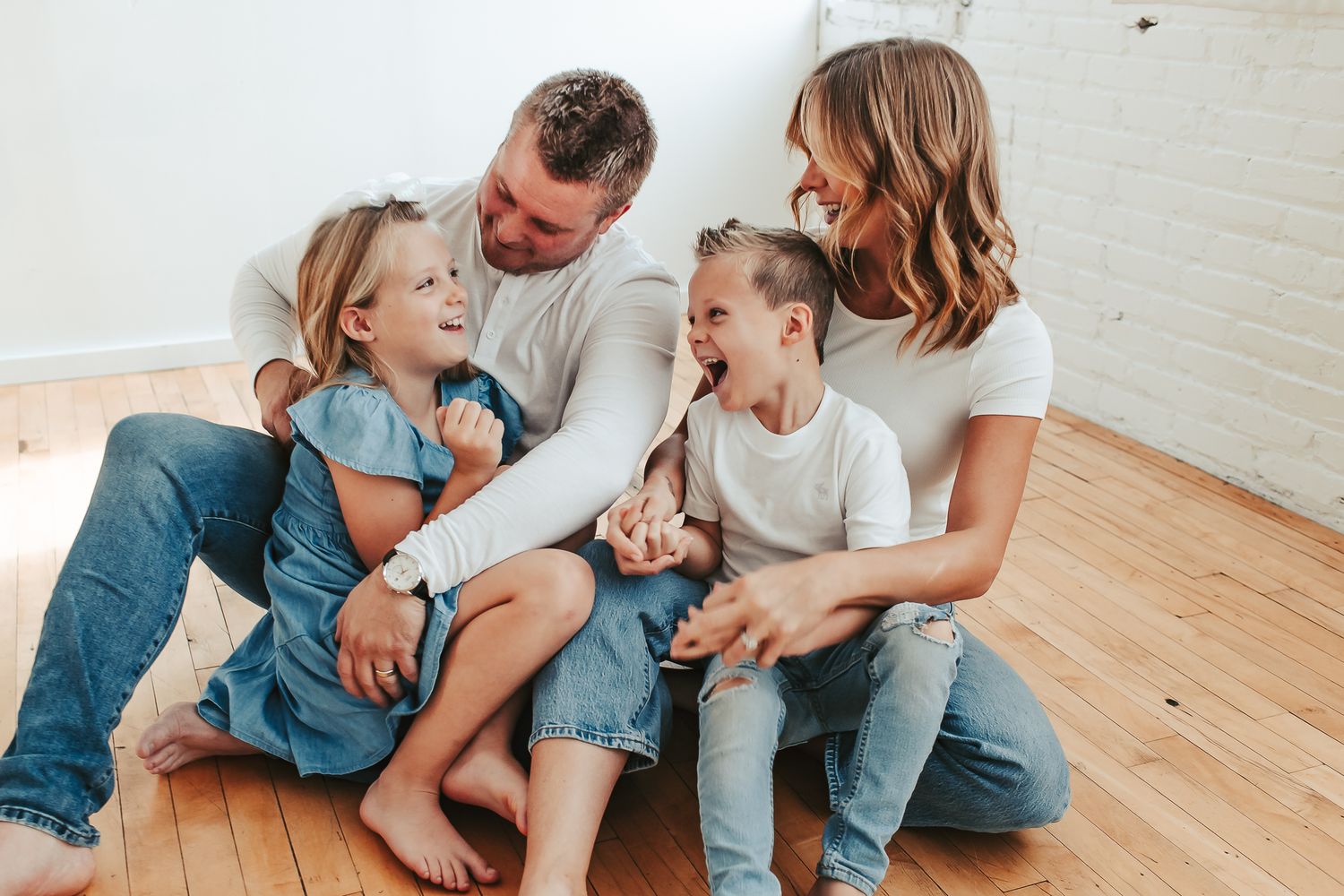A casual indoor family photoshoot on hardwood floors showing playful interaction and connection.