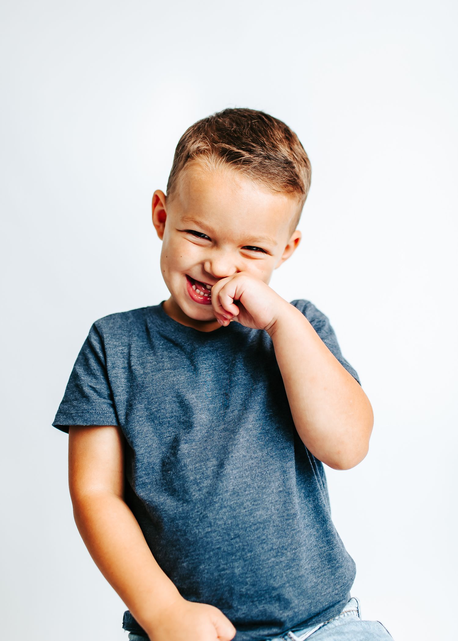 Child in grey t-shirt making silly expressions against white background.