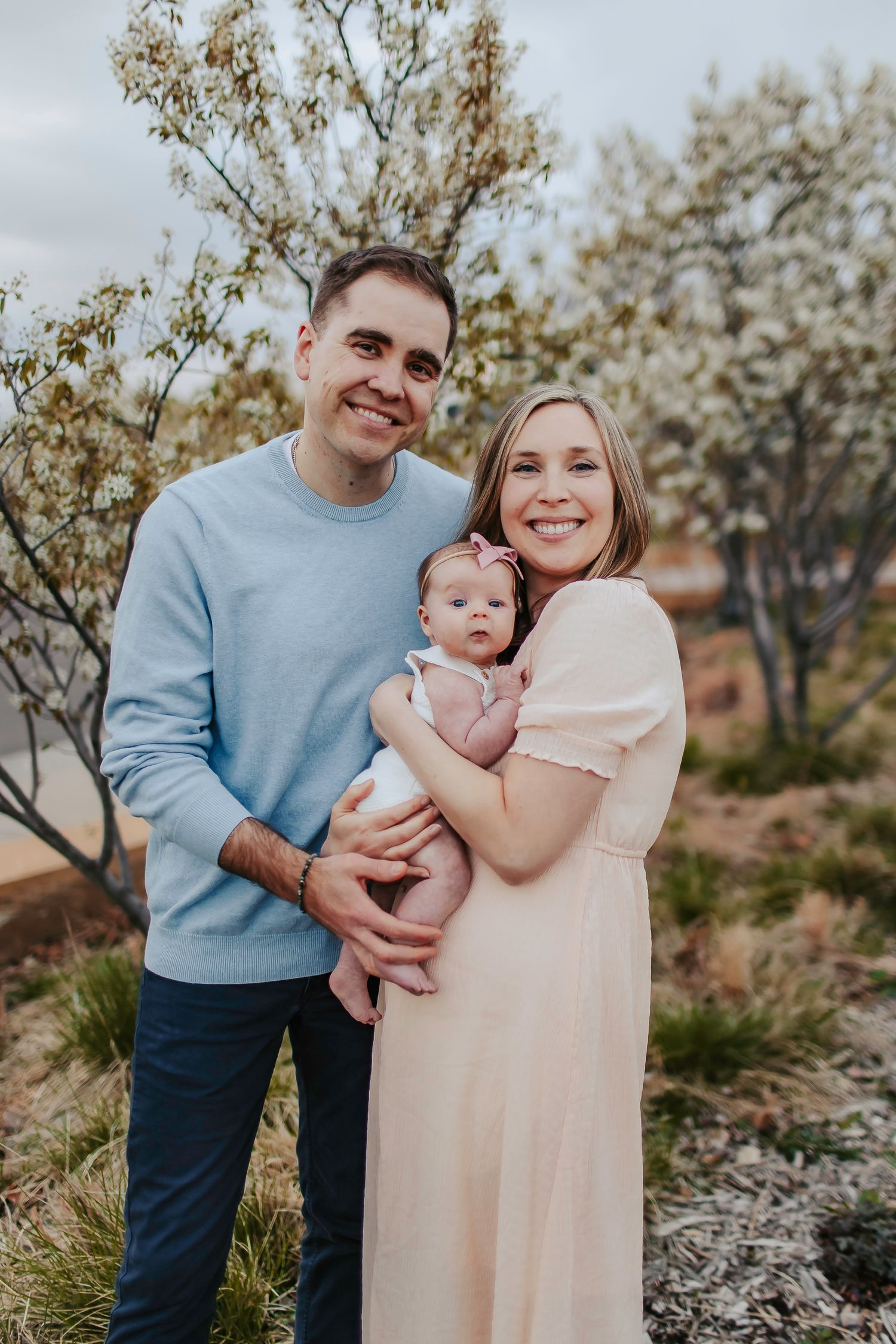 Family portrait session among blooming spring trees with soft pastel colors.