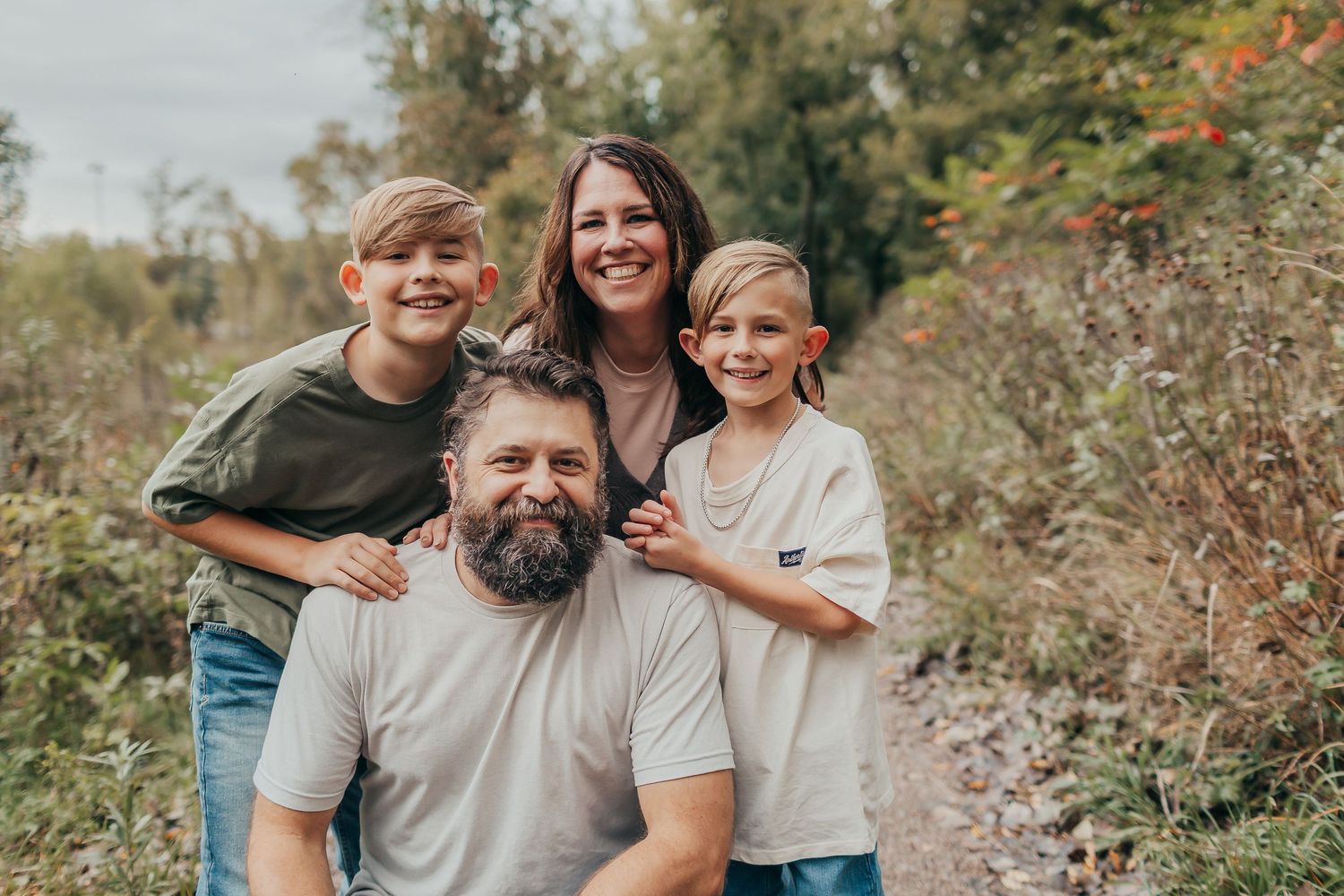 Family of four poses outdoors together against autumn foliage backdrop.