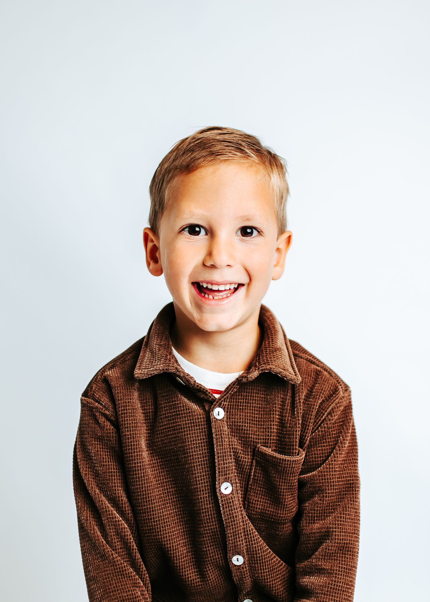 A child wearing a brown collared sweater shows a big cheerful smile against a light background.