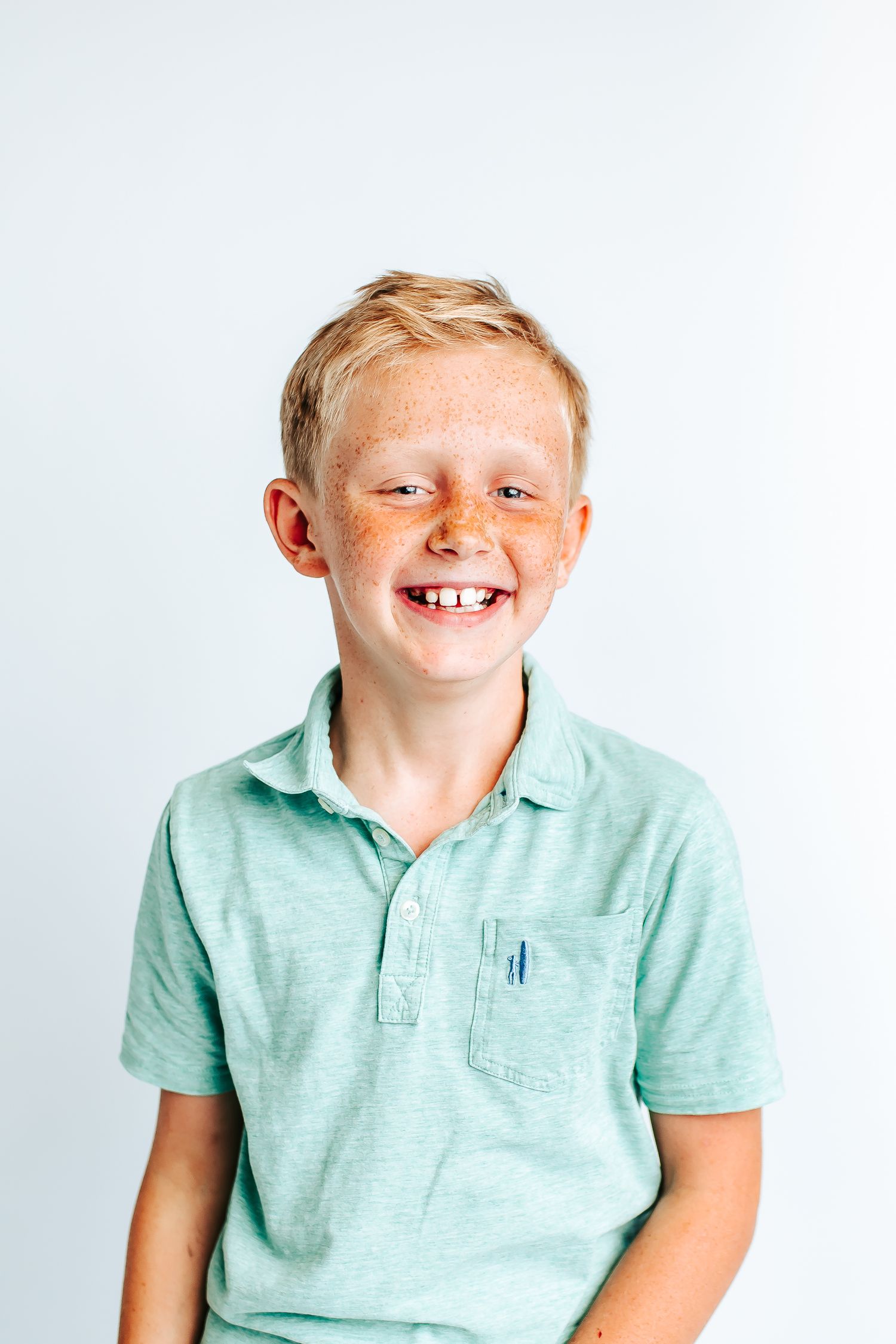 Child wearing mint green polo shirt smiling and laughing against white studio backdrop.
