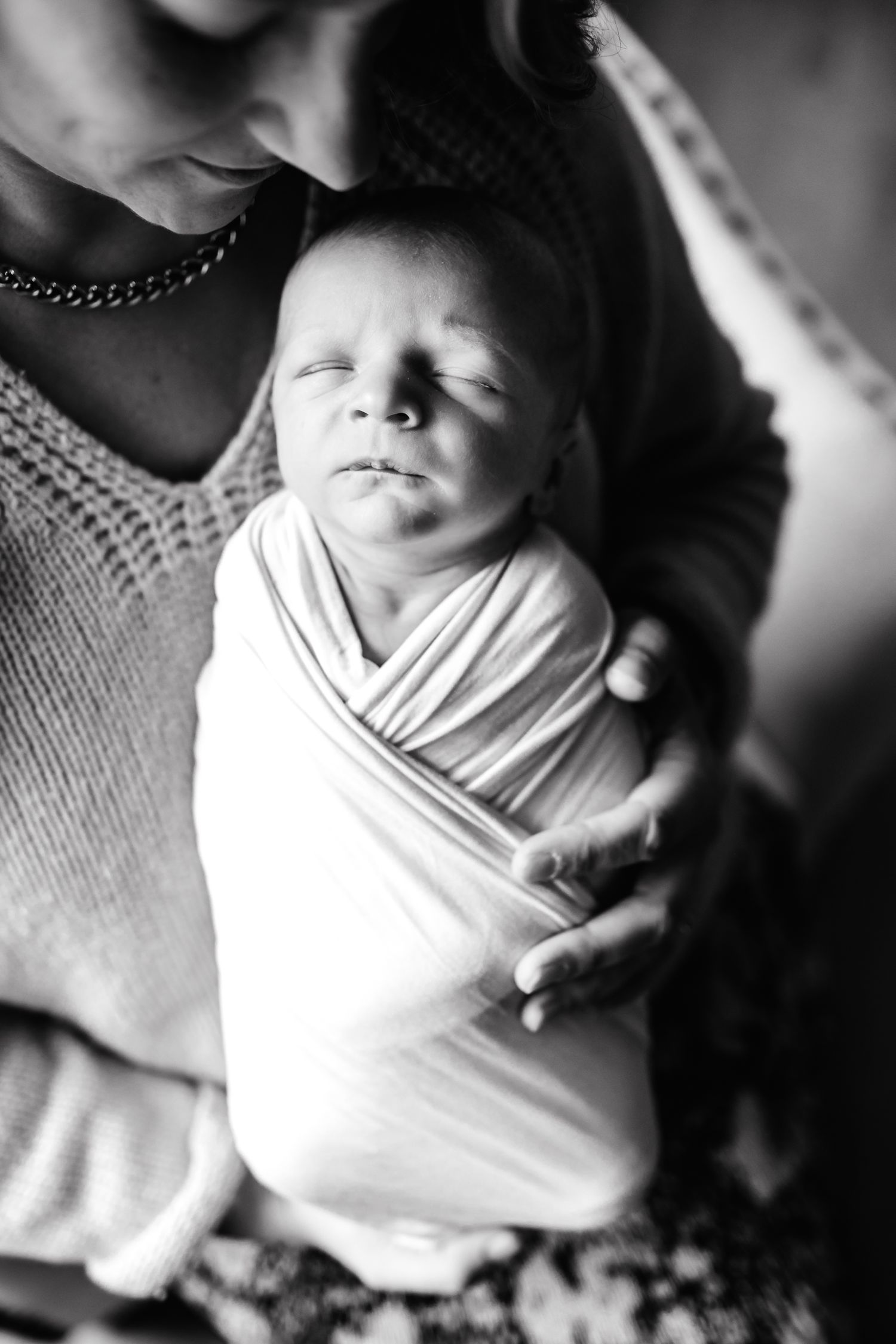 Black and white close-up portrait of infant being held in gentle embrace.