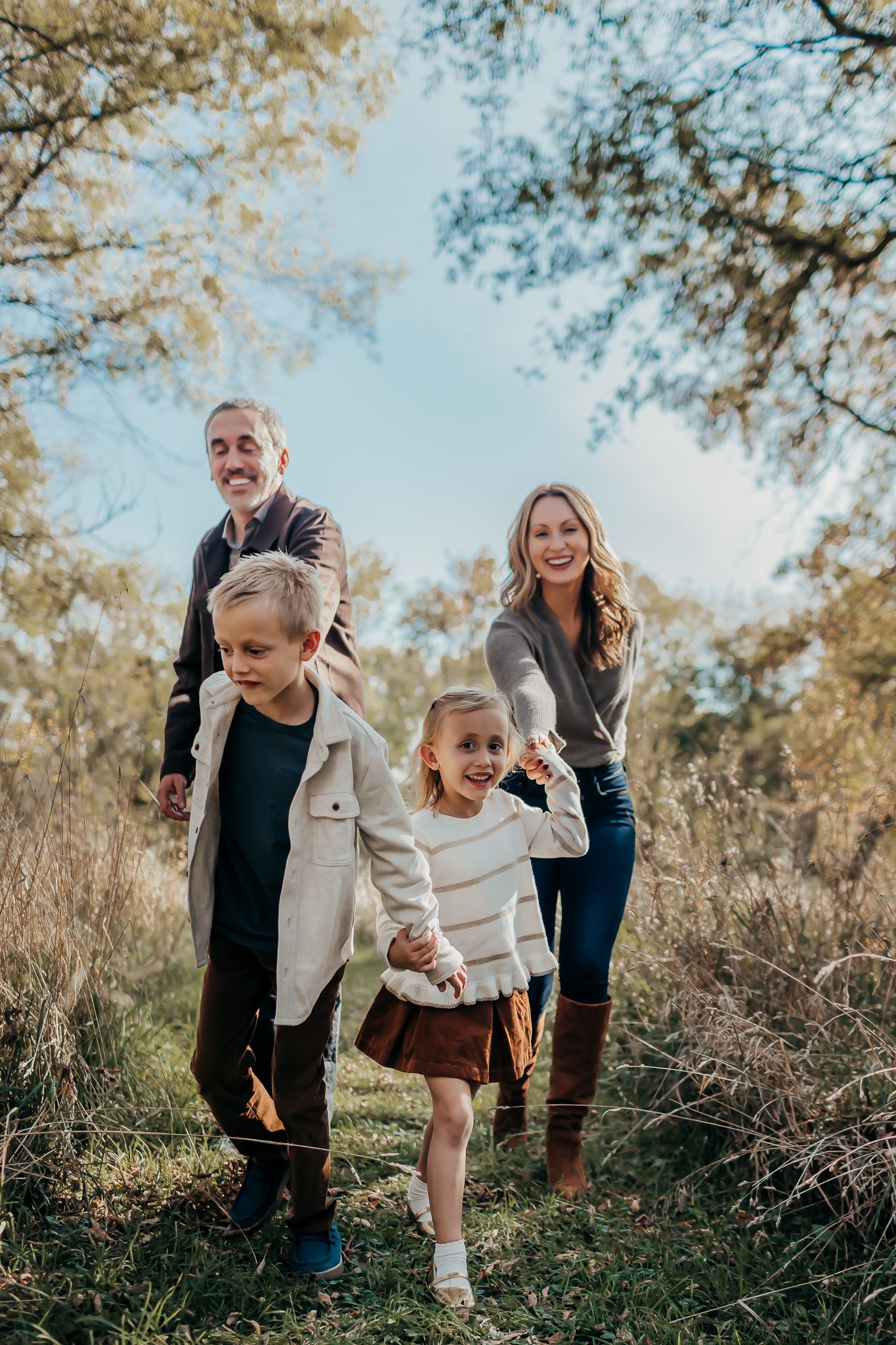 A playful outdoor family photoshoot in a field with golden autumn foliage.