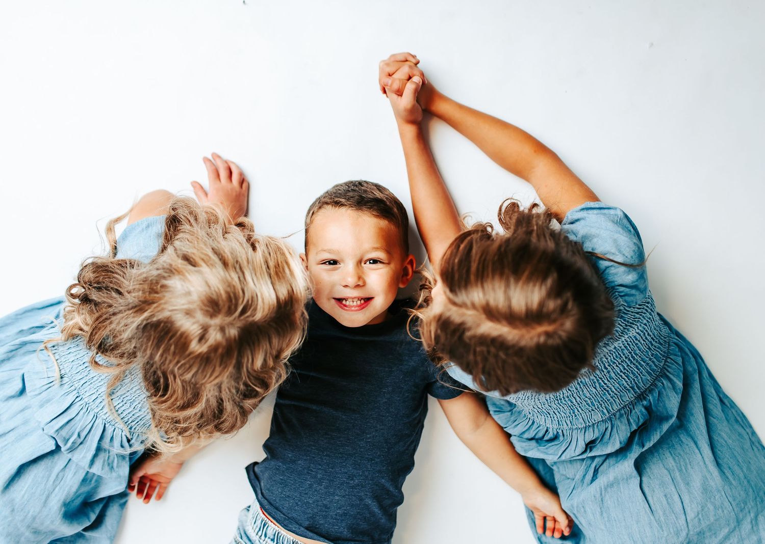 Four sequential photos of children lying down and laughing together in blue outfits.