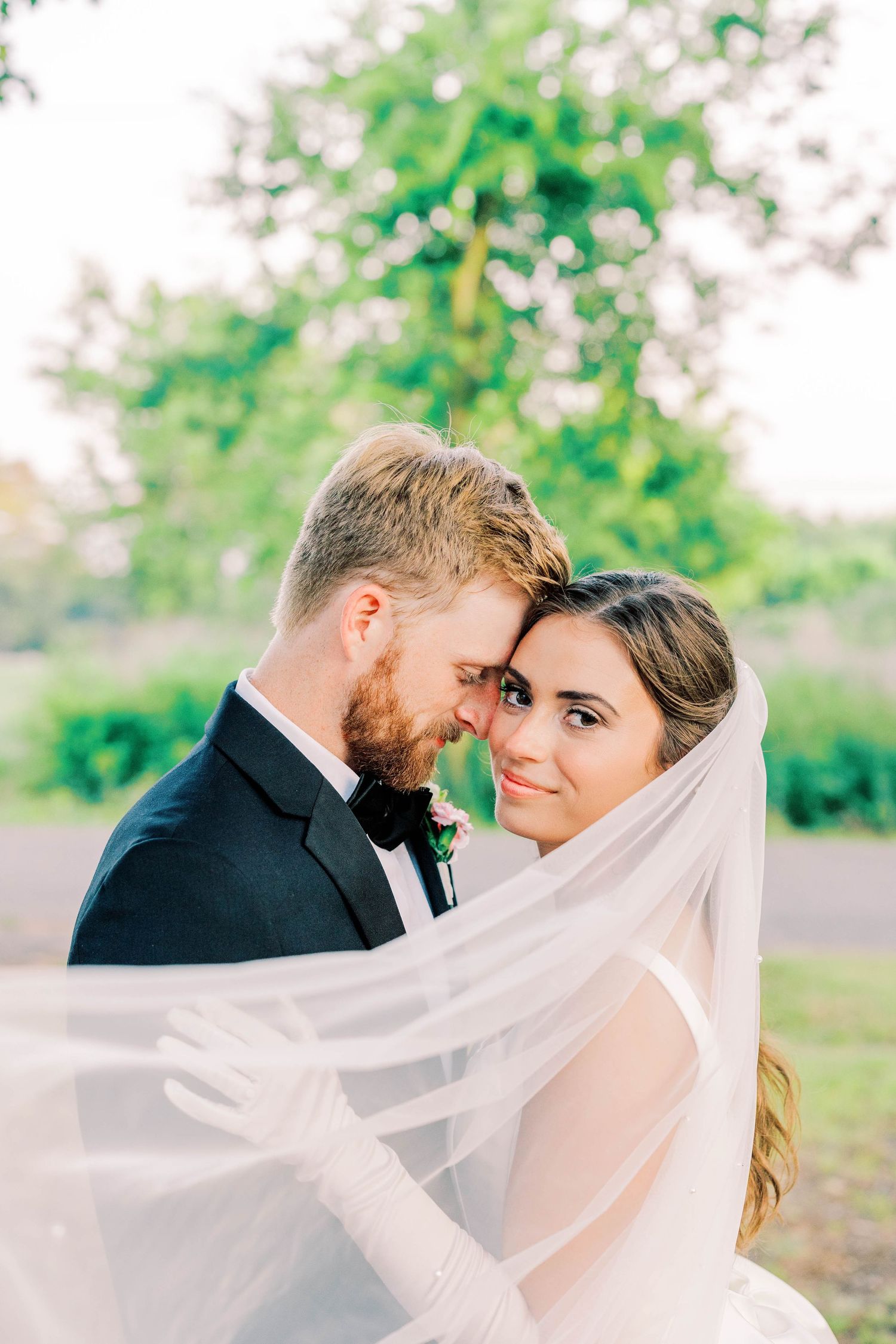 An intimate wedding portrait with flowing veil against natural greenery background.