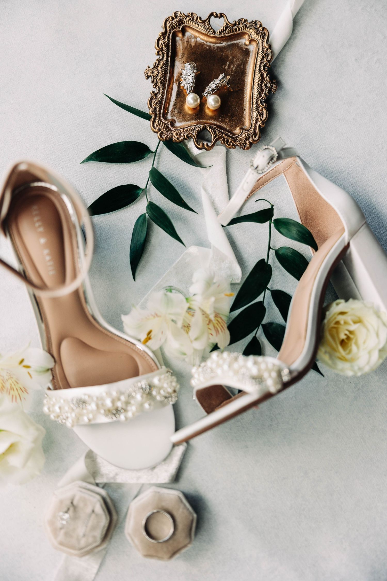 Bridal accessories including embellished heels and jewelry displayed with white roses.